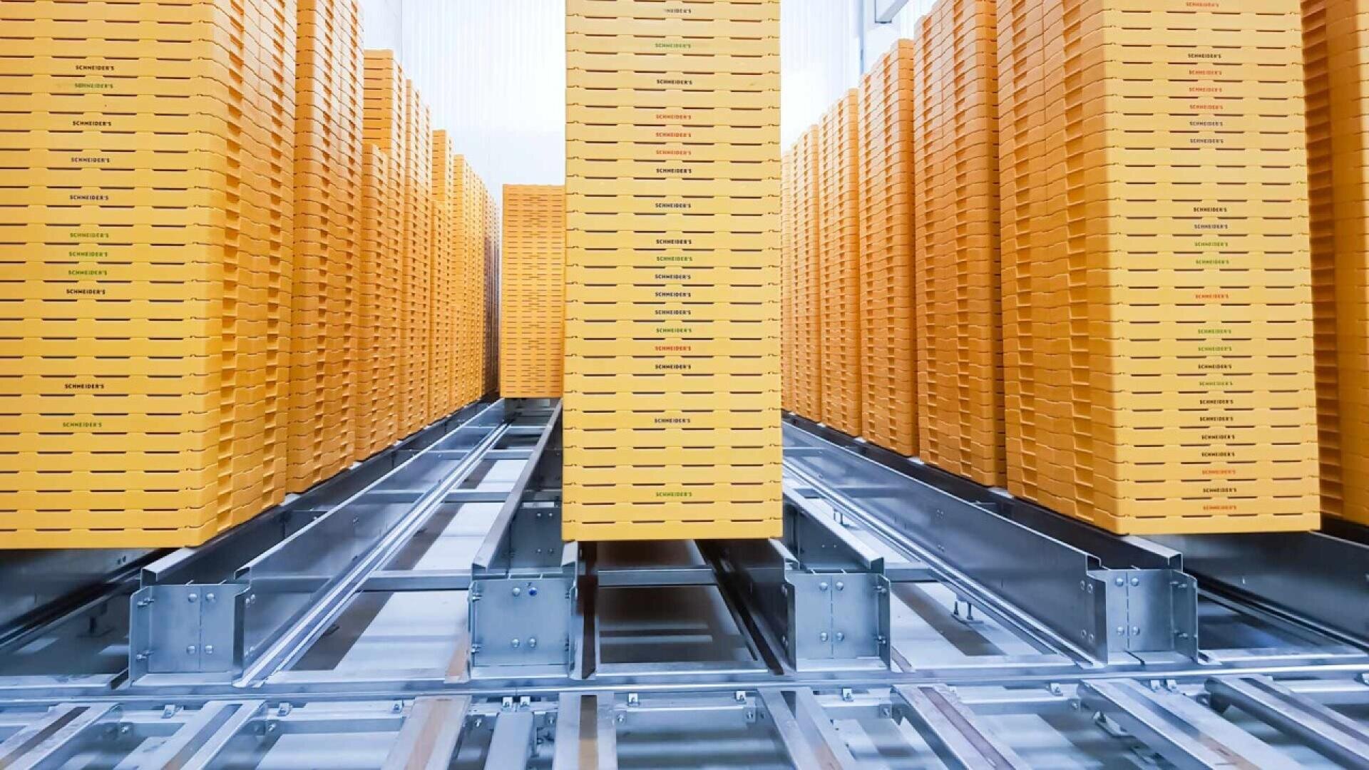 Tall stacks of yellow-orange boxes are neatly arranged in rows on metal tracks in a warehouse or industrial setting, creating a symmetrical, organized pattern.