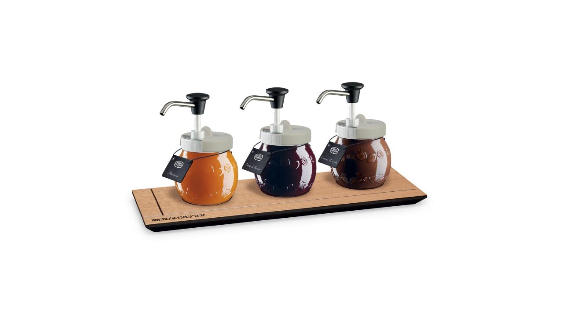 Three glass jars with metal pump dispensers, each containing different colored liquids, are placed on a wooden tray. Each jar has a black tag hanging from the lid. The jars are neatly arranged in a row.