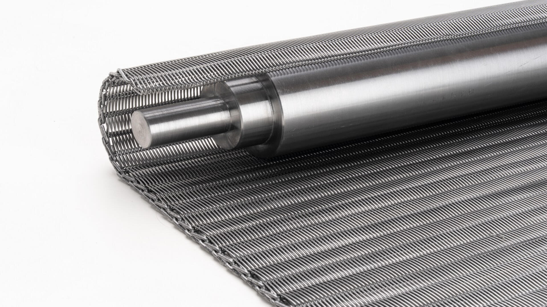 A close-up of a rolled metal wire mesh conveyor belt with a cylindrical metal rod as the roller, displayed on a white background.