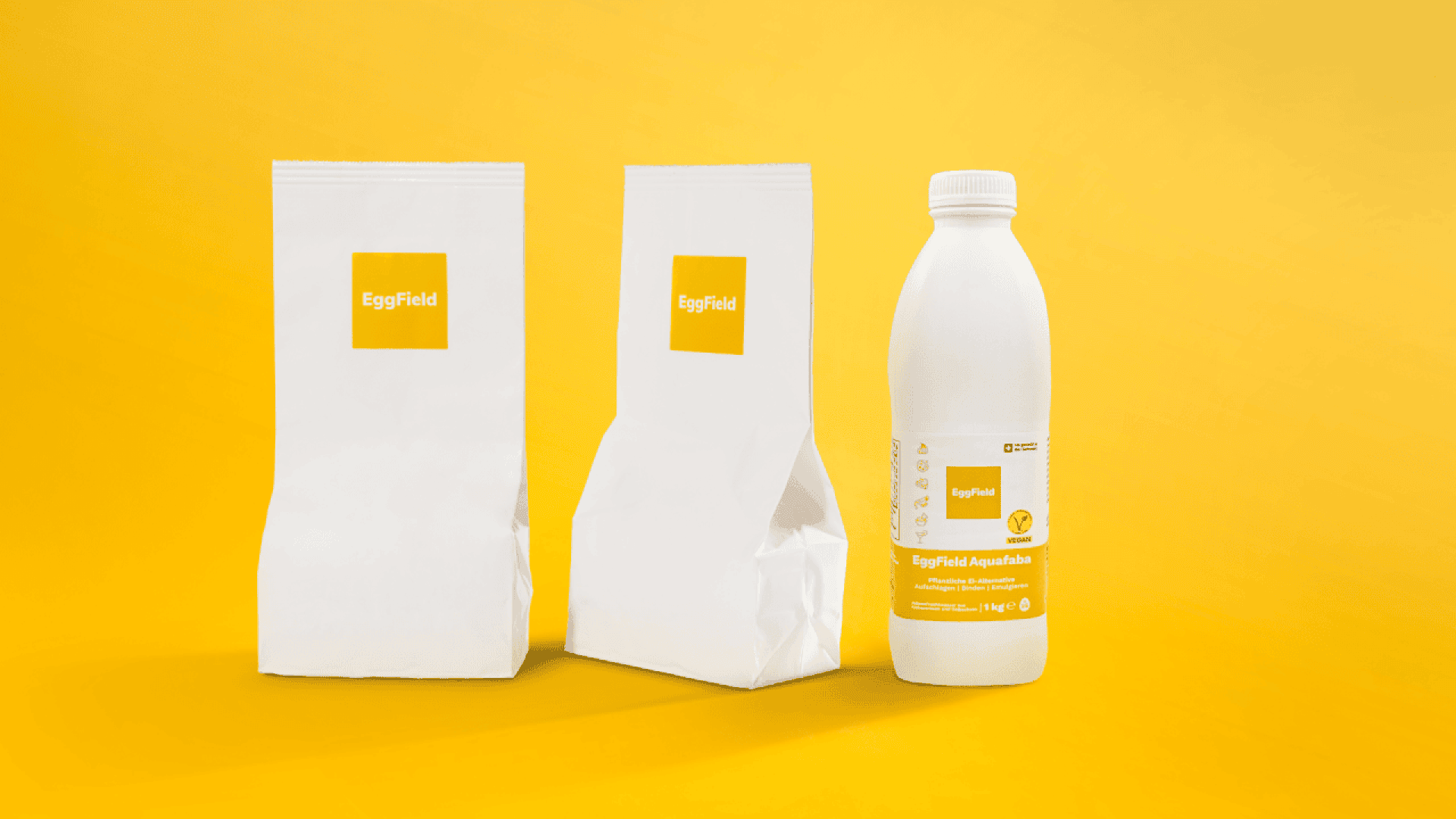 Three EggField products on a yellow background: two white paper bags with yellow EggField labels and one white plastic bottle with a yellow label displaying product information.