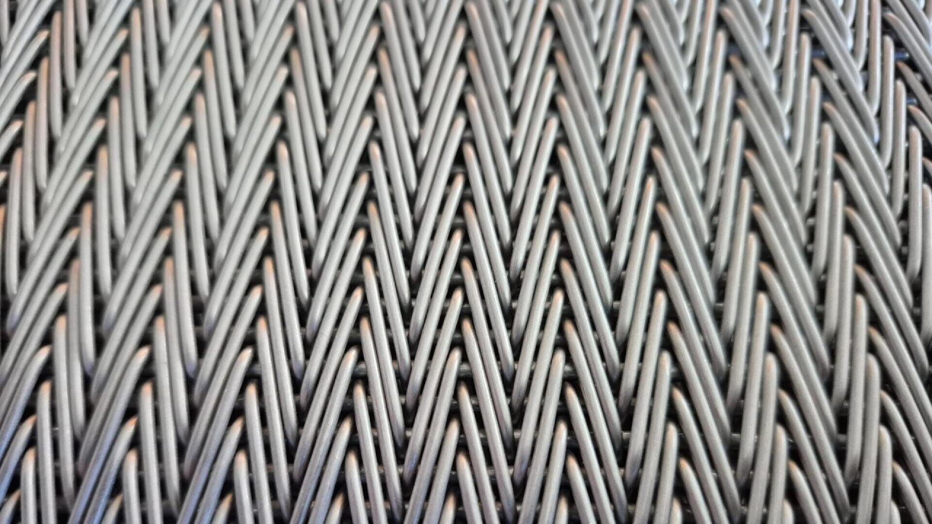 Close-up of a woven pattern featuring dark, tightly interlaced strands arranged in a V-shaped, chevron design, creating a textured, repetitive geometric appearance.