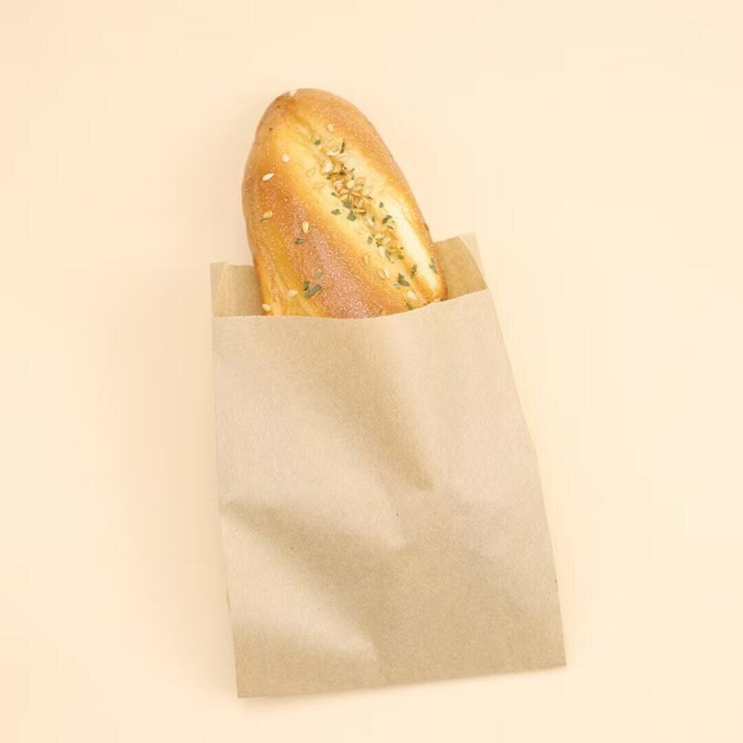 A baguette with seeds on top is partially inside a plain brown paper bag, set against a beige background.