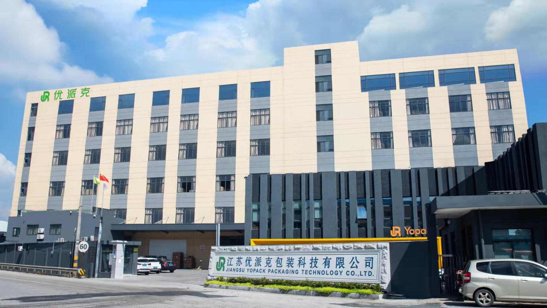 A modern multi-story industrial building with beige and grey exterior, large windows, and signage reading Jiangsu Yopack Packaging Technology Co., Ltd. A company logo and flag are visible at the entrance.