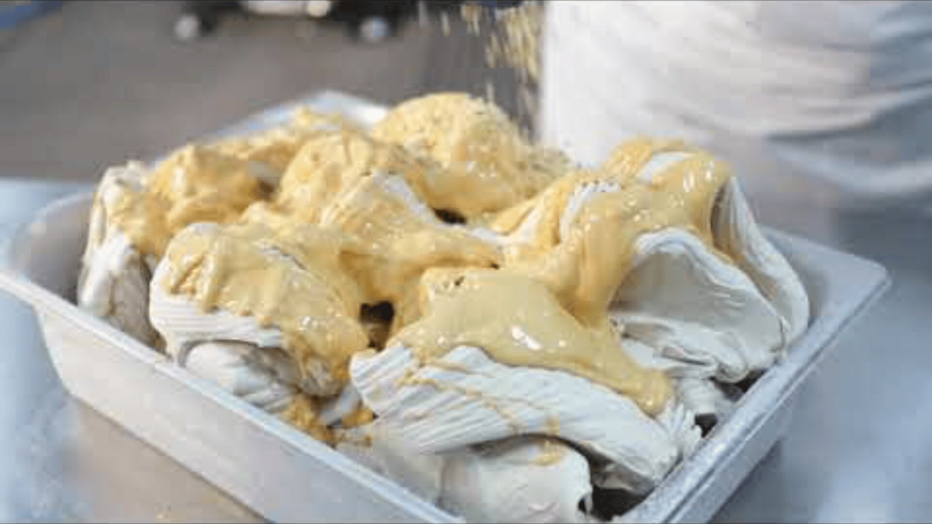 A metal container filled with creamy, white ice cream is covered with a thick, golden sauce, sprinkled with crushed nuts on top.