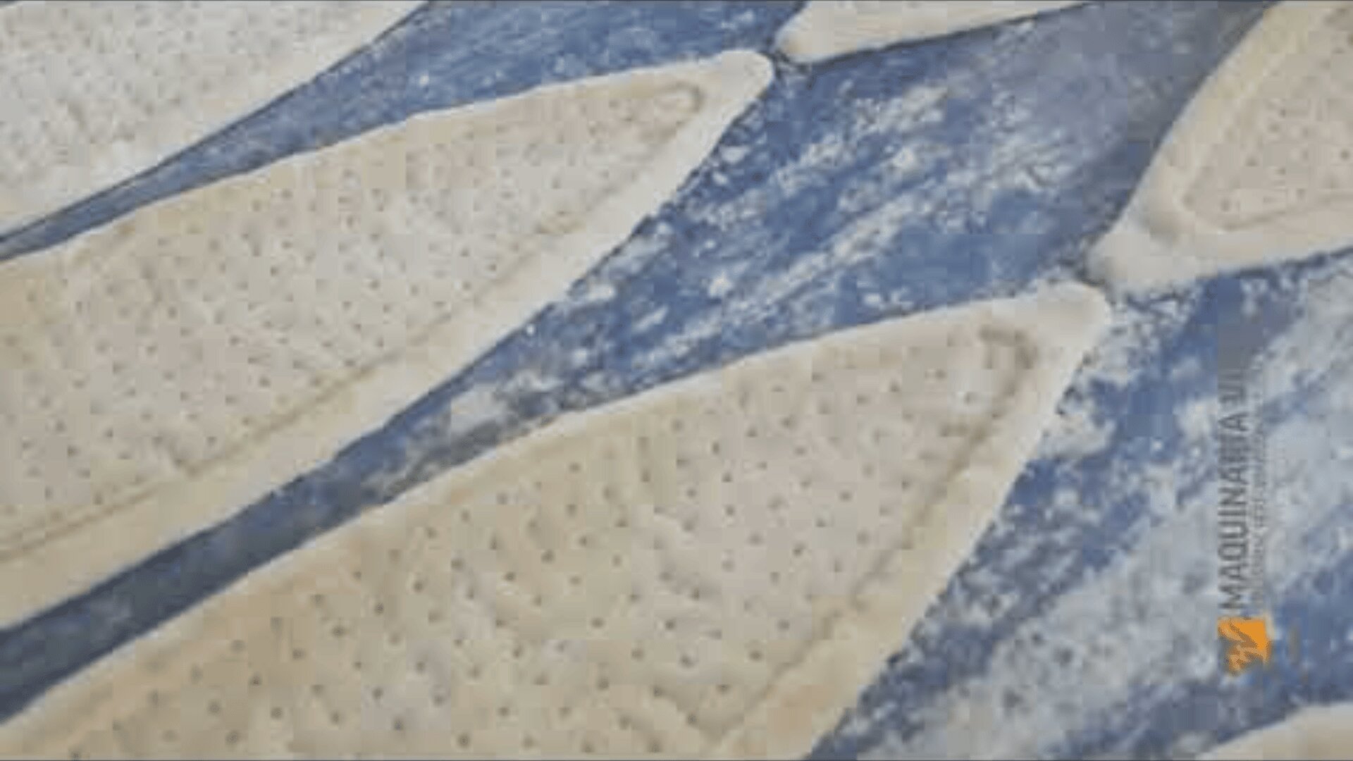 Close-up of several raw, oval pieces of dough with a perforated surface on a floured blue work surface, ready for baking.
