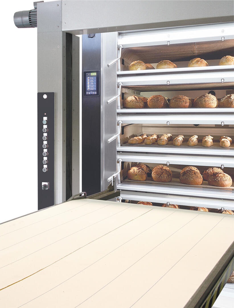 Ein kommerzieller Brotofen mit mehreren Einschüben, die jeweils mit runden Brotlaiben gefüllt sind, neben einer leeren Förderfläche zum Be- und Entladen von Brot.