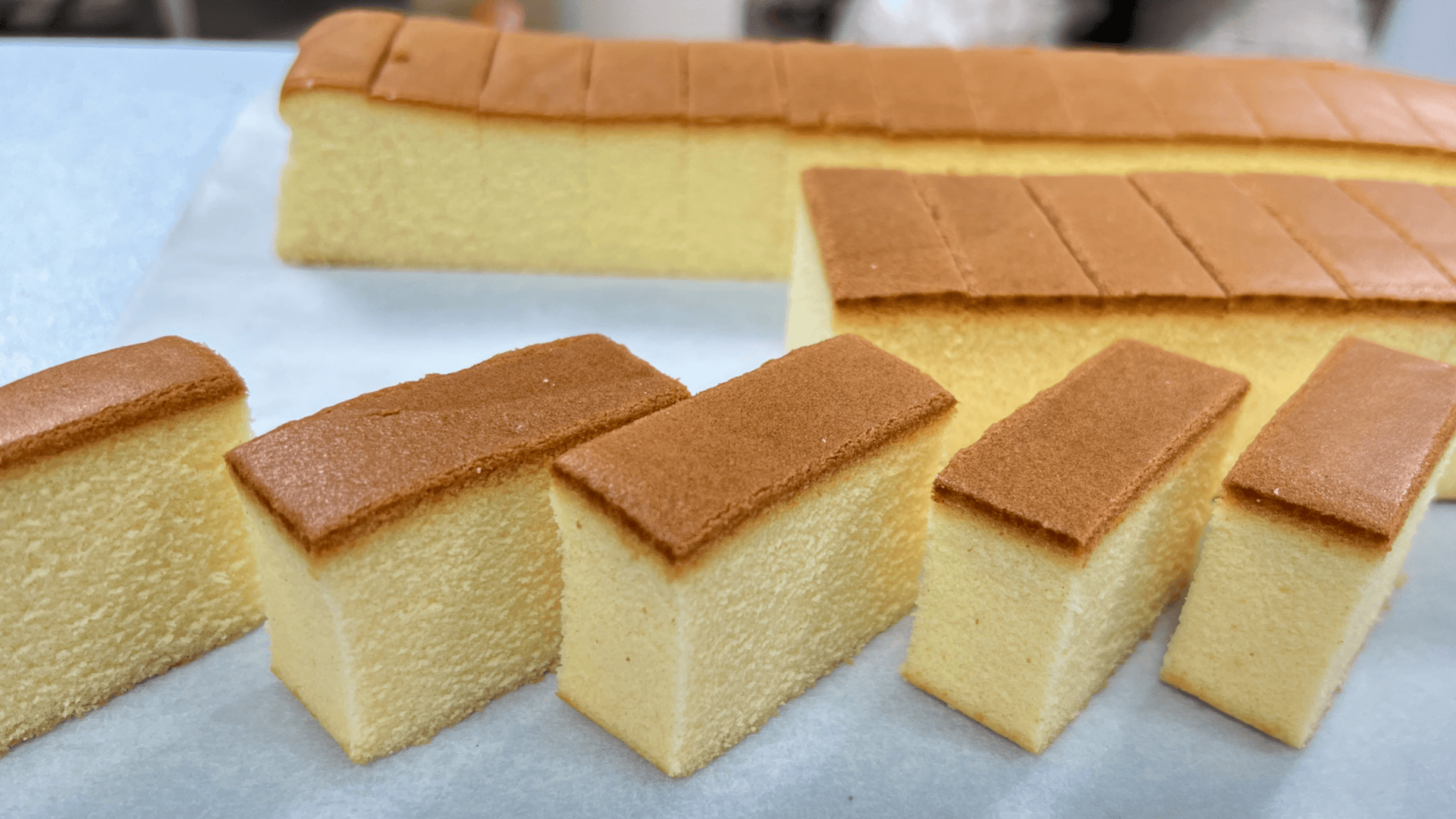 Sliced pieces of fluffy, golden-brown sponge cake arranged on a white surface, with a larger uncut portion of the cake in the background.