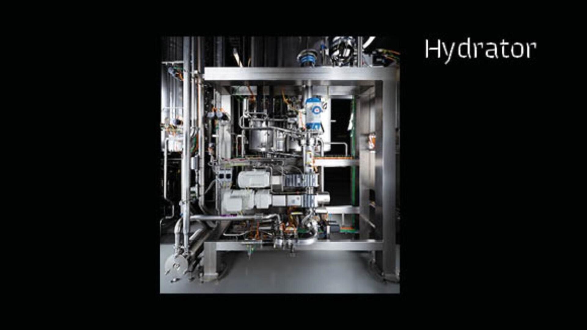 A large, industrial stainless steel machine labeled Hydrator with numerous pipes, valves, and components, set against a black background.