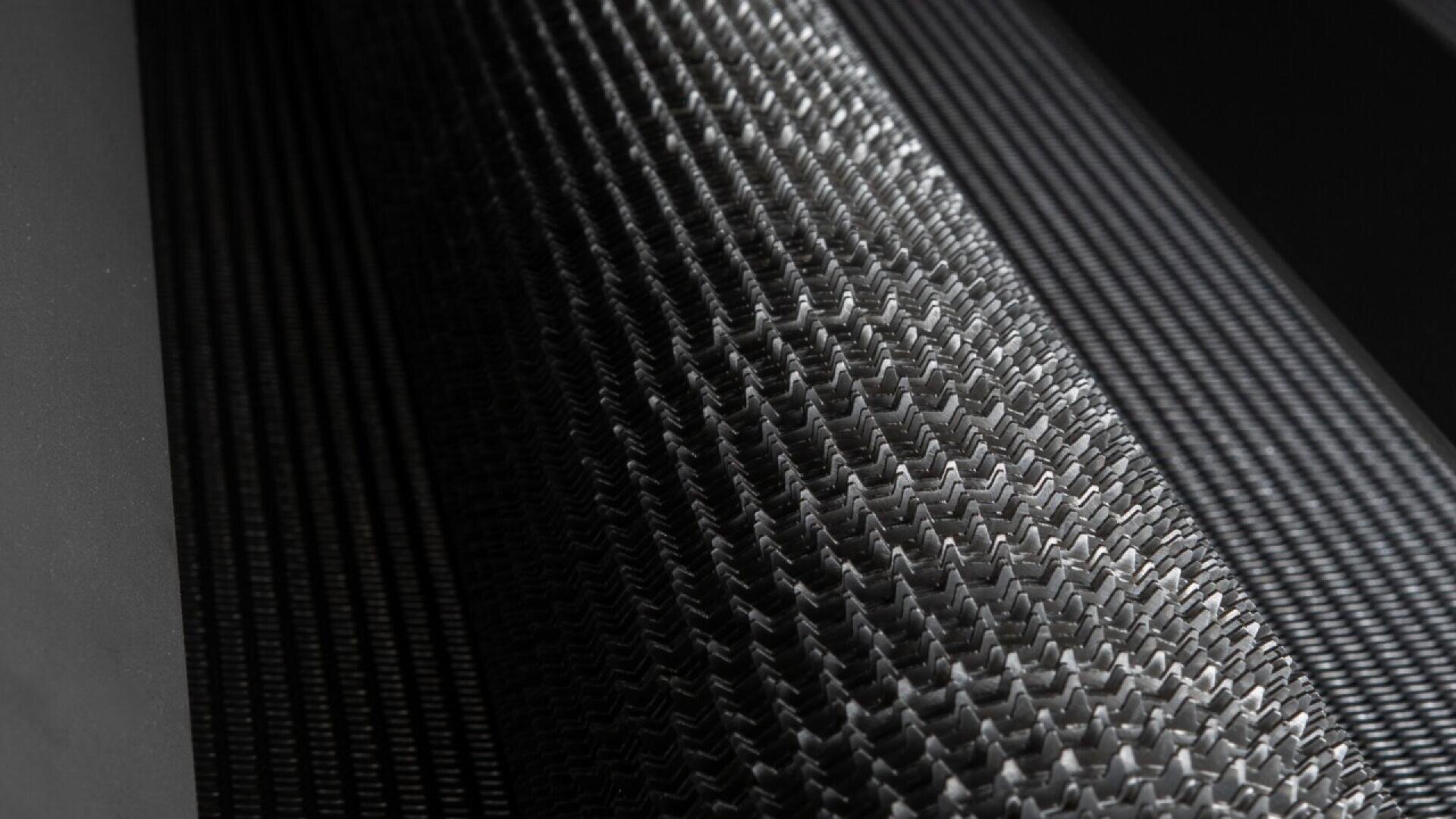 Close-up of interlocking, zigzagged metal gears or rollers with a textured, repeating pattern in an industrial setting. The lighting highlights the shiny metallic surfaces and intricate details.