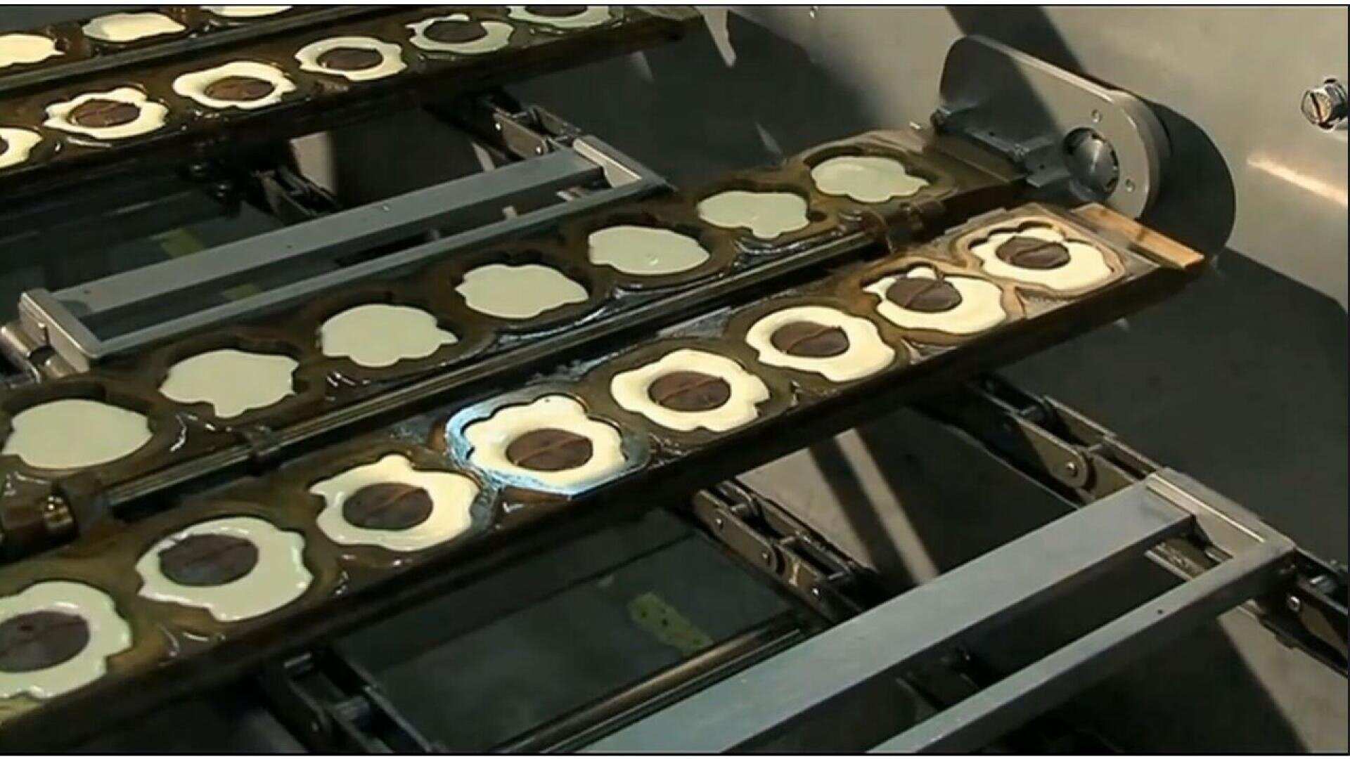 Rows of flower-shaped cookie molds filled with dough and chocolate centers are lined up on a conveyor belt in a factory setting, ready for baking or further processing.