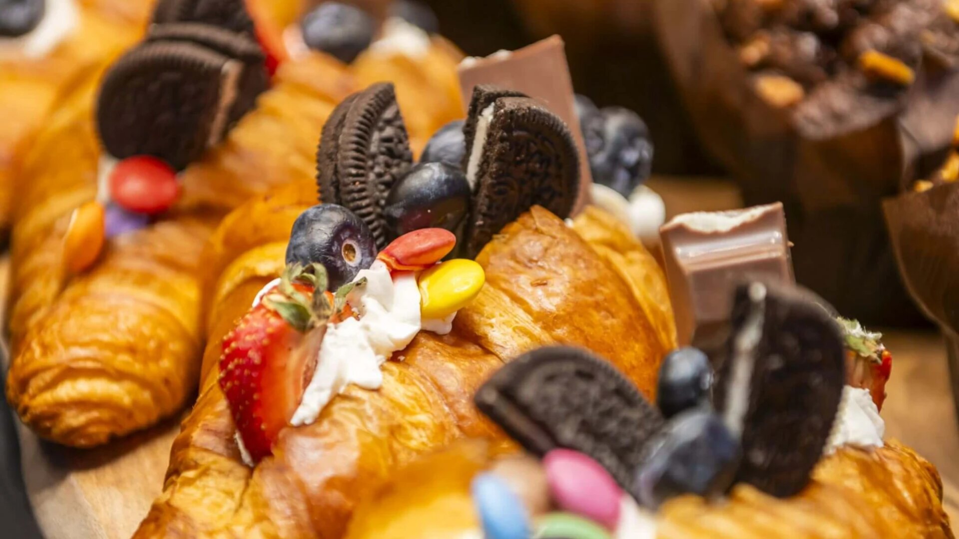 Nahaufnahme von Croissants, die mit Schlagsahne, Blaubeeren, Erdbeeren, Schokoladenstückchen, Oreo-Keksen und bunten Pralinen überzogen sind.