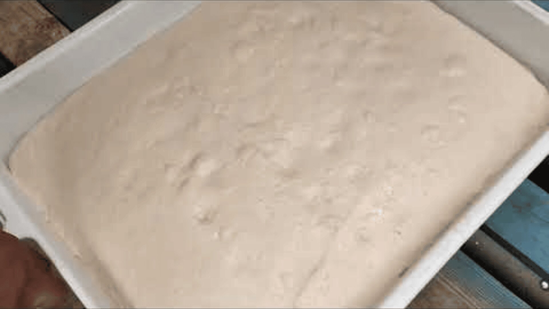 A large, rectangular container filled with risen bread dough showing bubbles and a smooth, slightly uneven surface.