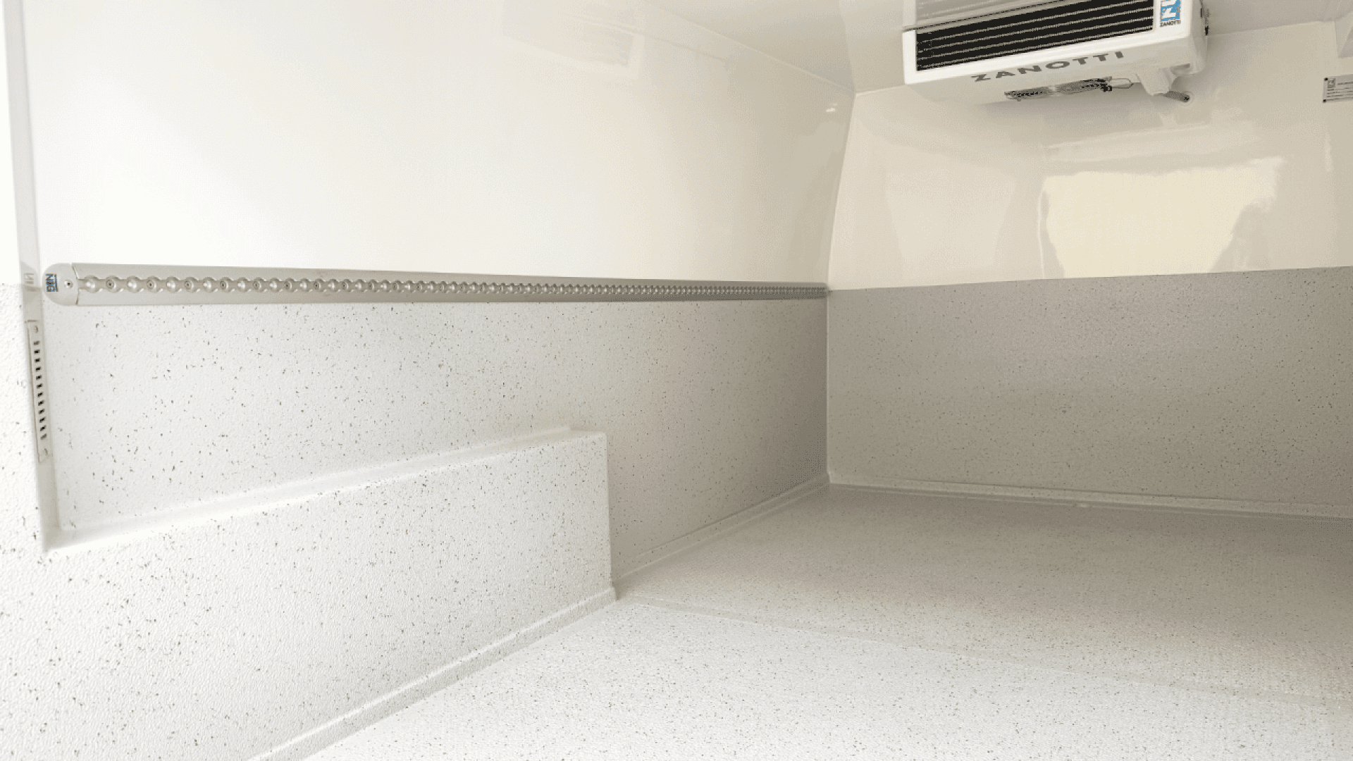 The image shows the clean, empty interior of a refrigerated van with white, speckled insulated walls and floor, and a cooling unit mounted on the upper right wall.