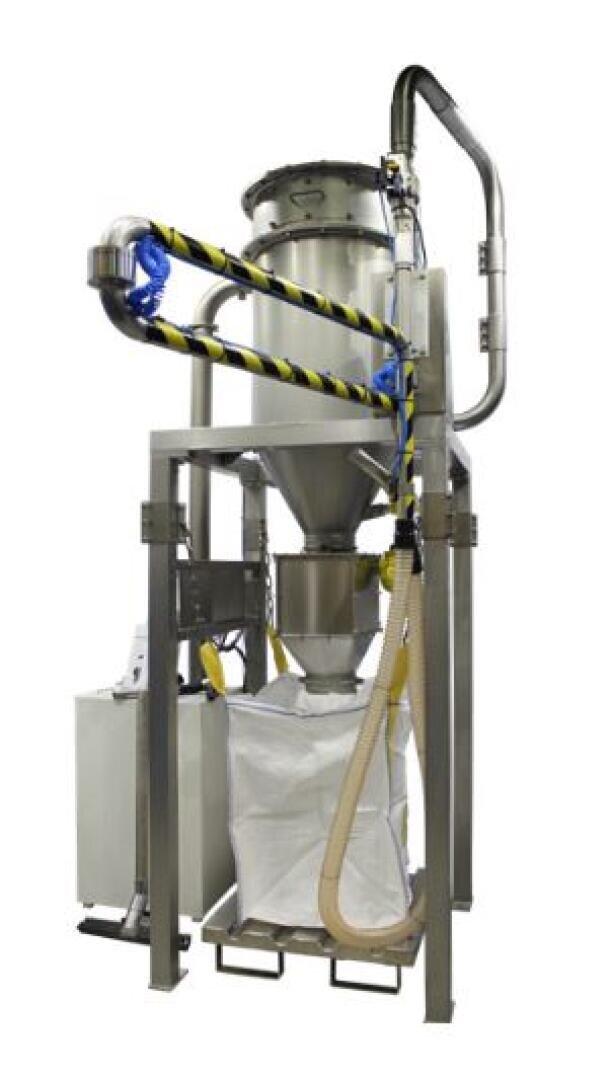 Eine große Industriemaschine mit einem Metallrahmen, einem zylindrischen Behälter, Rohren und Schläuchen, die Material in einen weißen Sack abgibt, der auf einer Palette unter dem Gerät steht. Einige Rohre sind mit Sicherheitsband umwickelt.