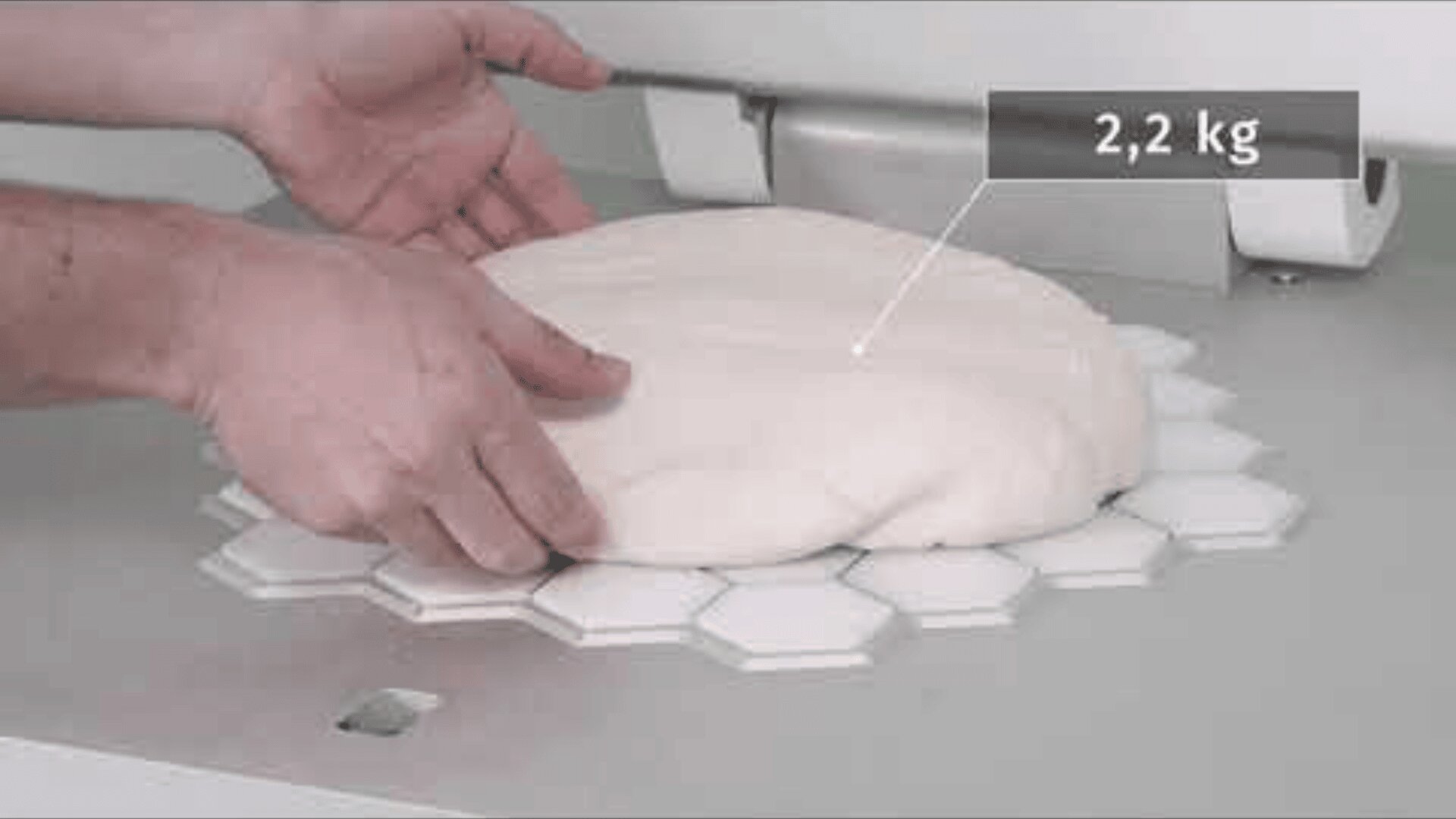 A person places a 2.2 kg piece of dough on a hexagonal surface and probably prepares it for cutting or dividing in a commercial kitchen.