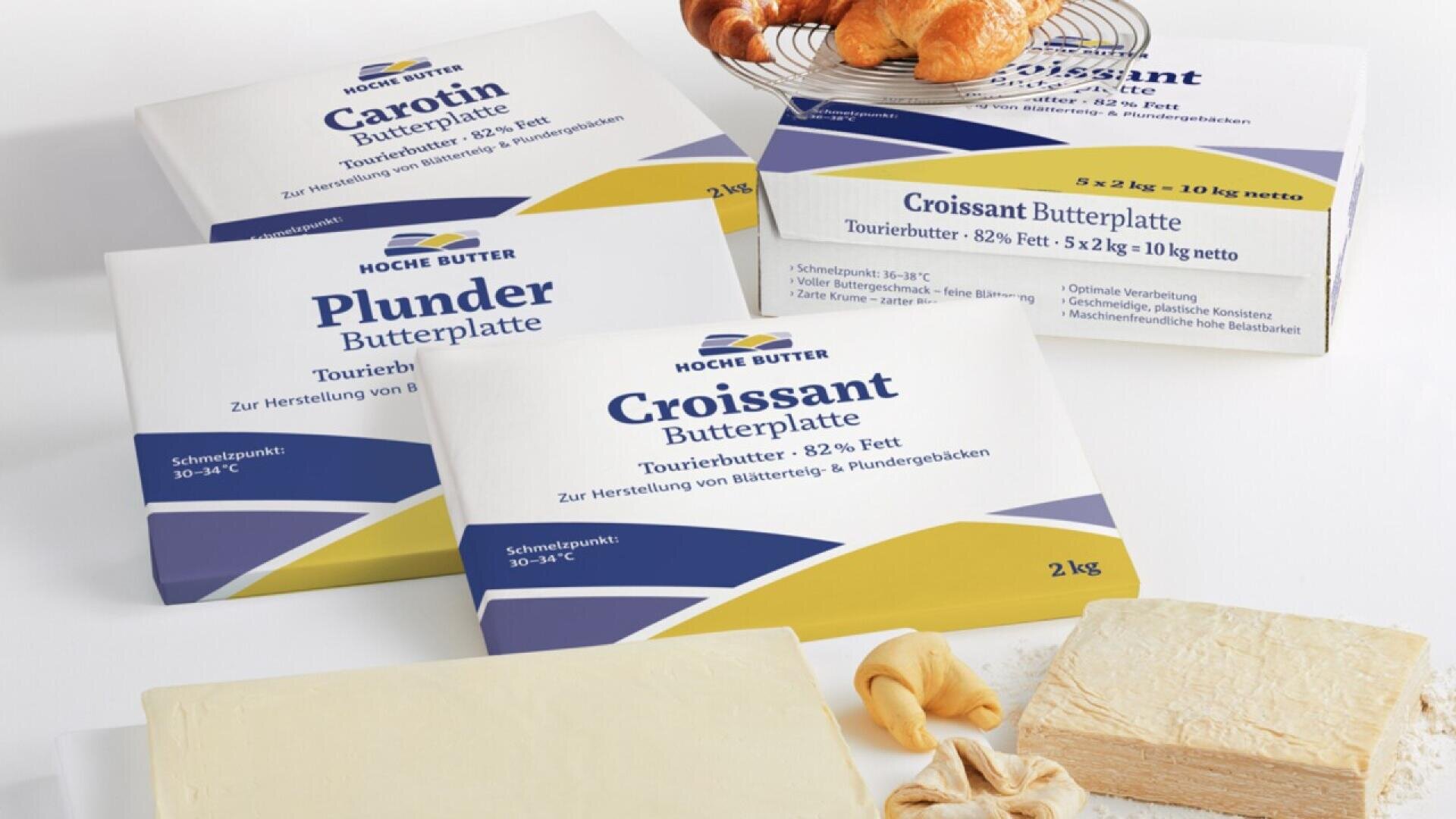 Four rectangular packages of Hoche Butter labeled for baking (Carotin, Plunder, Croissant) sit beside unwrapped butter blocks and pastries, including croissants, on a white surface.