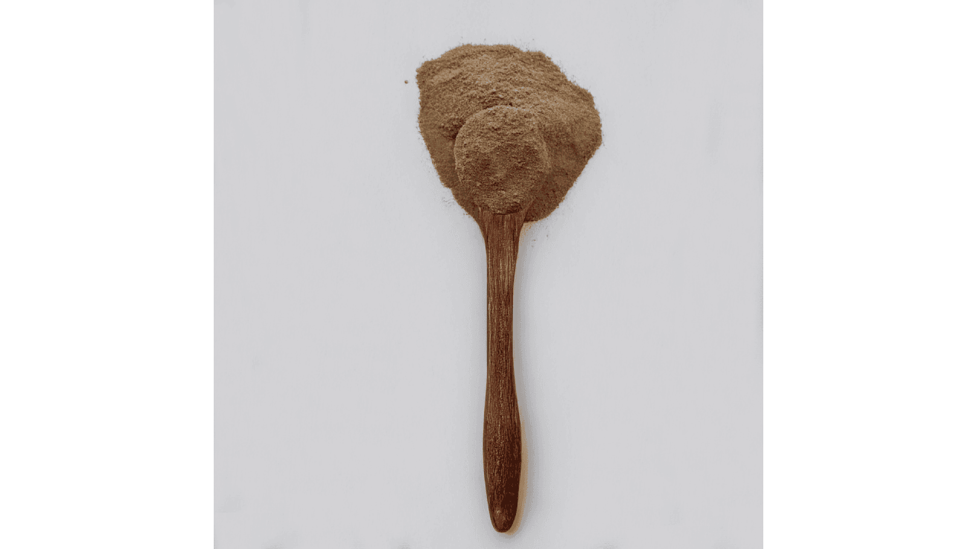 Ein Holzlöffel gefüllt mit braunem Pulver, oben herum ist noch mehr Pulver verschüttet, auf weißem Hintergrund.