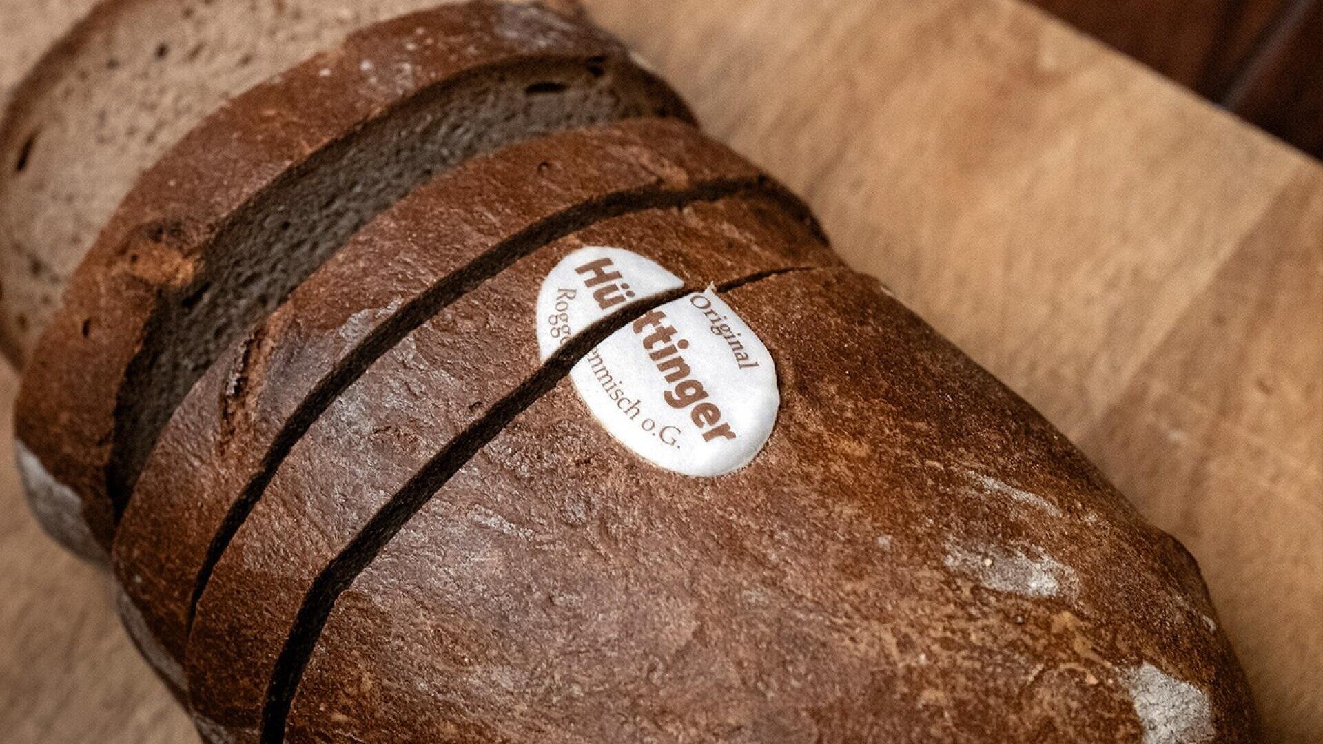 A loaf of dark rye bread partially sliced on a wooden surface, with a round Original Hüttringer label on the crust.
