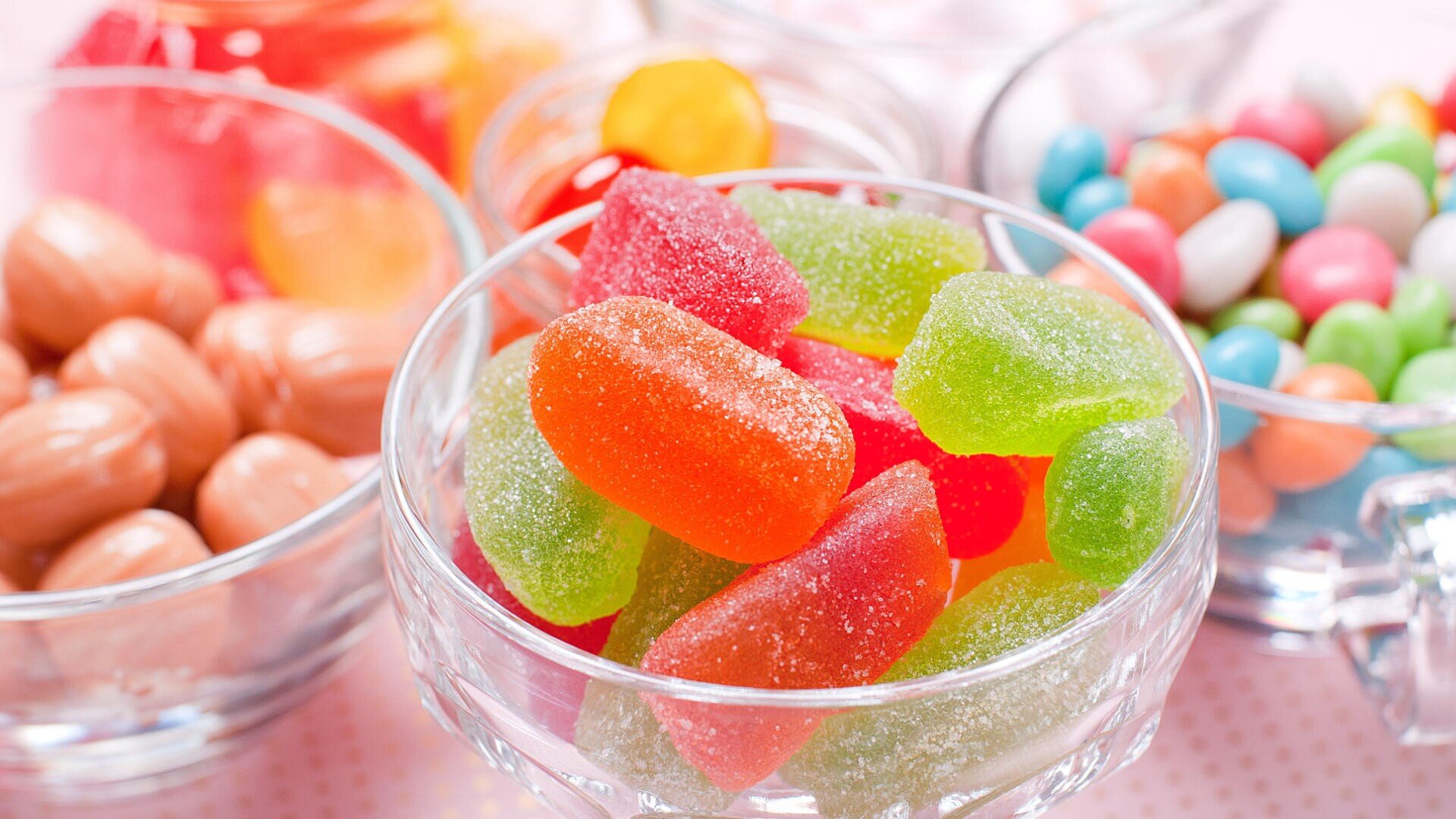 Colorful assorted candies including sugar-coated jelly candies, hard candies, and candy-coated chocolates displayed in clear glass bowls.