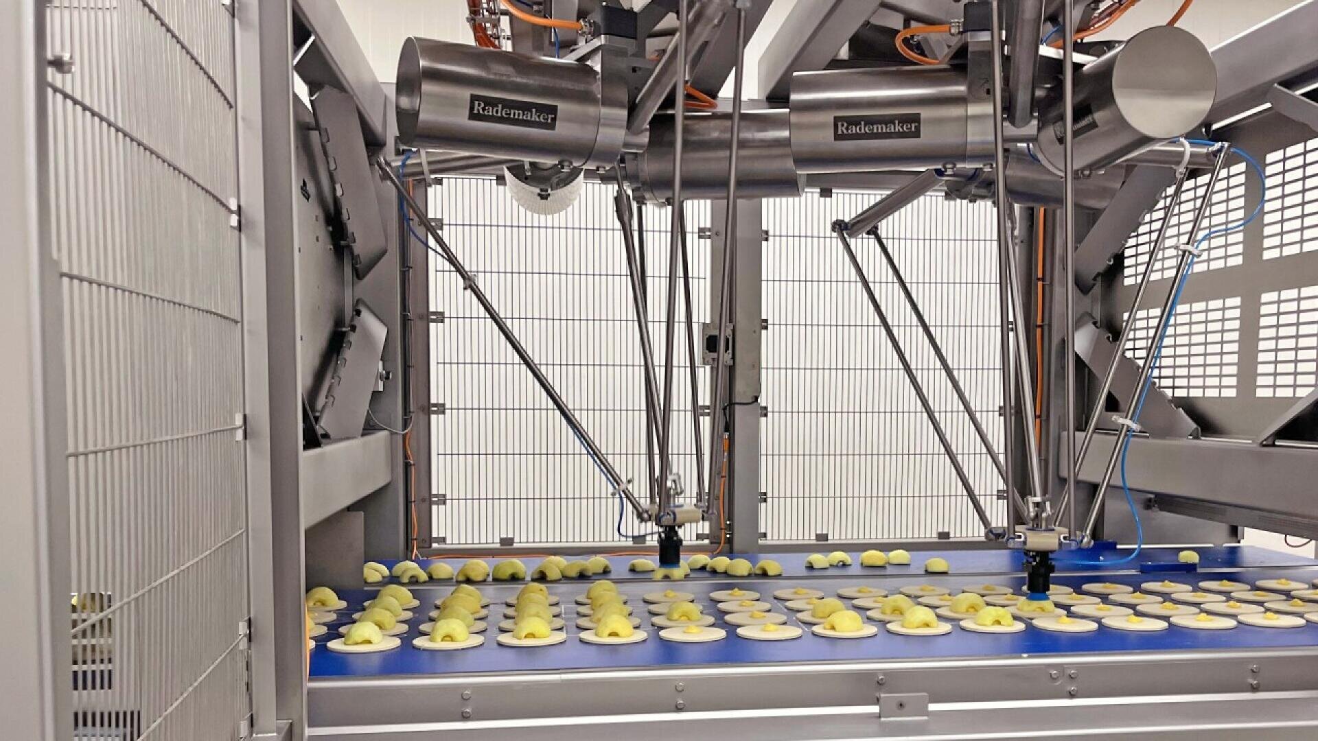 Roboterarme in einer Fabrik automatisieren den Prozess des Auflegens von Füllungen auf runde Teigstücke auf einem Förderband und bereiten sie für die weitere Verarbeitung in einer Lebensmittelproduktionsanlage vor.