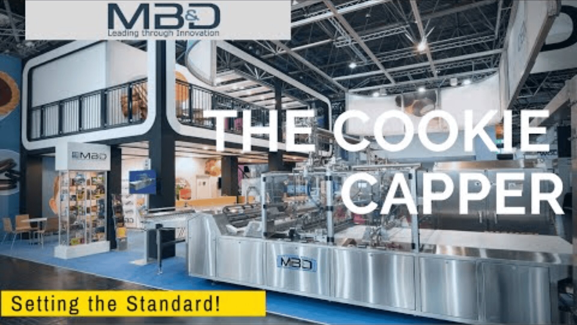 A modern exhibition stand shows the MB&D logo, a large industrial machine with the inscription THE COOKIE CAPPER and the slogan Setting the Standard! on a yellow banner in the bottom left-hand corner.