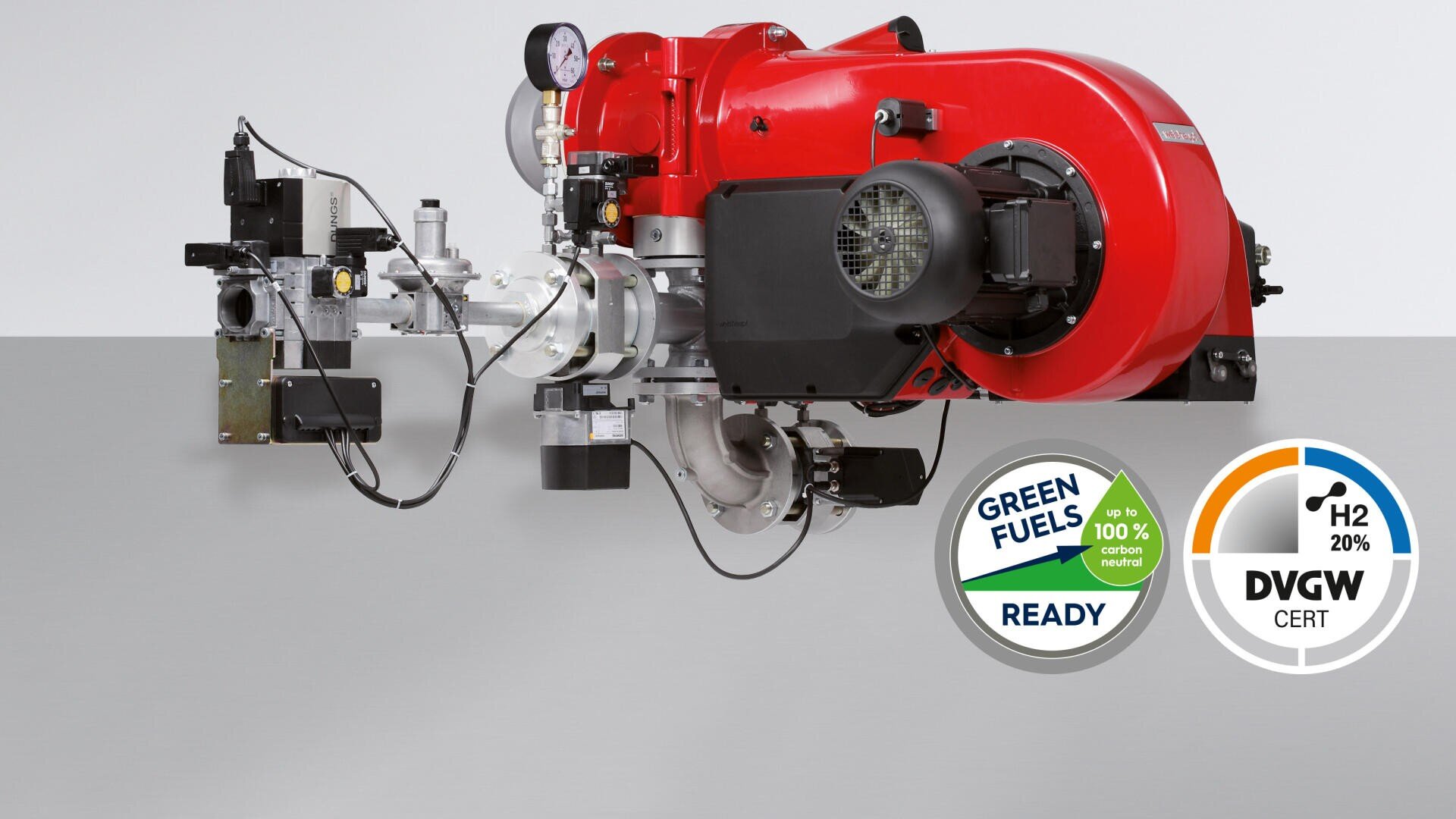 A large red industrial burner with connected measuring devices and components is shown. Two certification plates show the readiness for green fuels and up to 20 % hydrogen use, with DVGW certification.