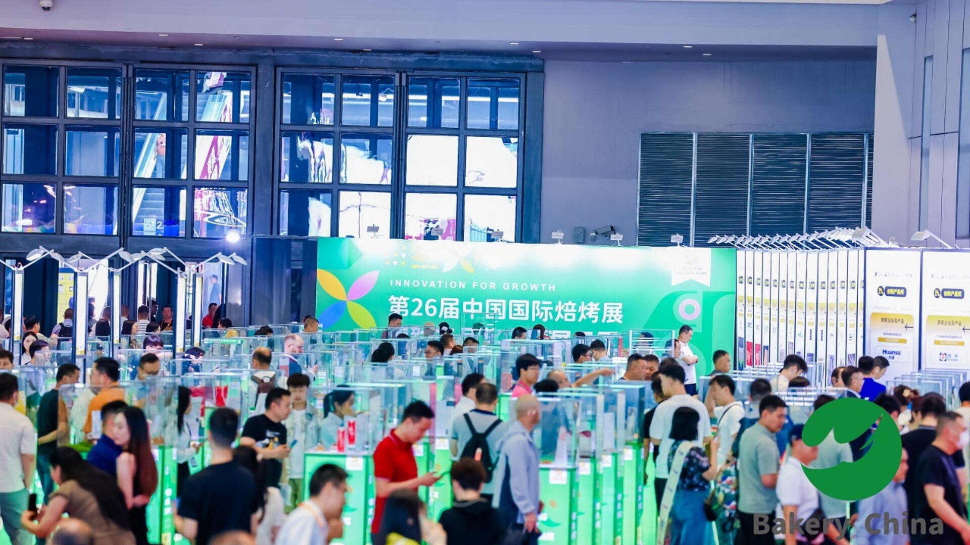 A busy exhibition hall with many people walking among glass displays, a large green banner reading “26th China International Baking Exhibition” in Chinese and English, and the Bakery China logo in the corner.