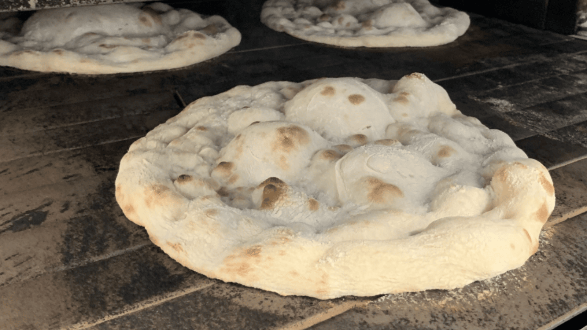 Three pieces of pizza dough with large bubbles and golden spots bake directly on the stone base of a pizza oven.