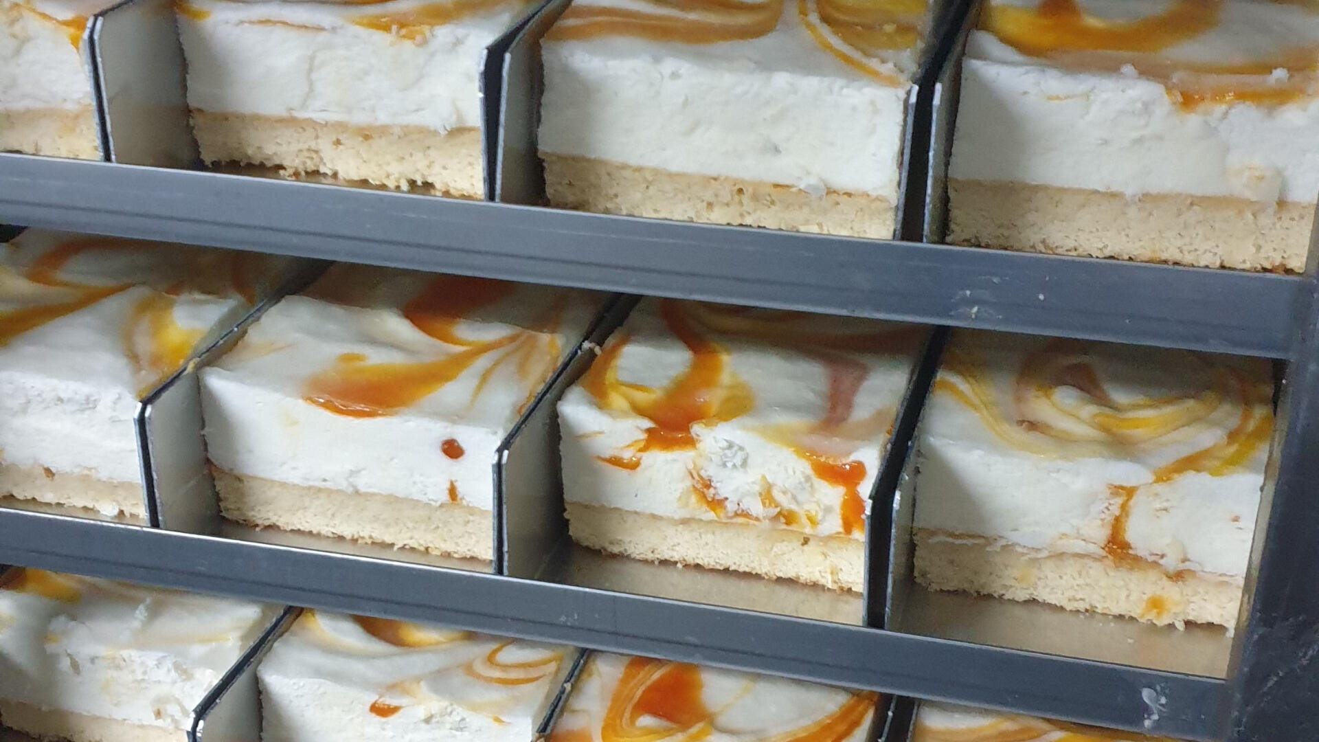 Mehrere Scheiben Käsekuchen mit Karamellwirbel und Kruste, fein säuberlich in Metallschalen mit Trennwänden angeordnet.