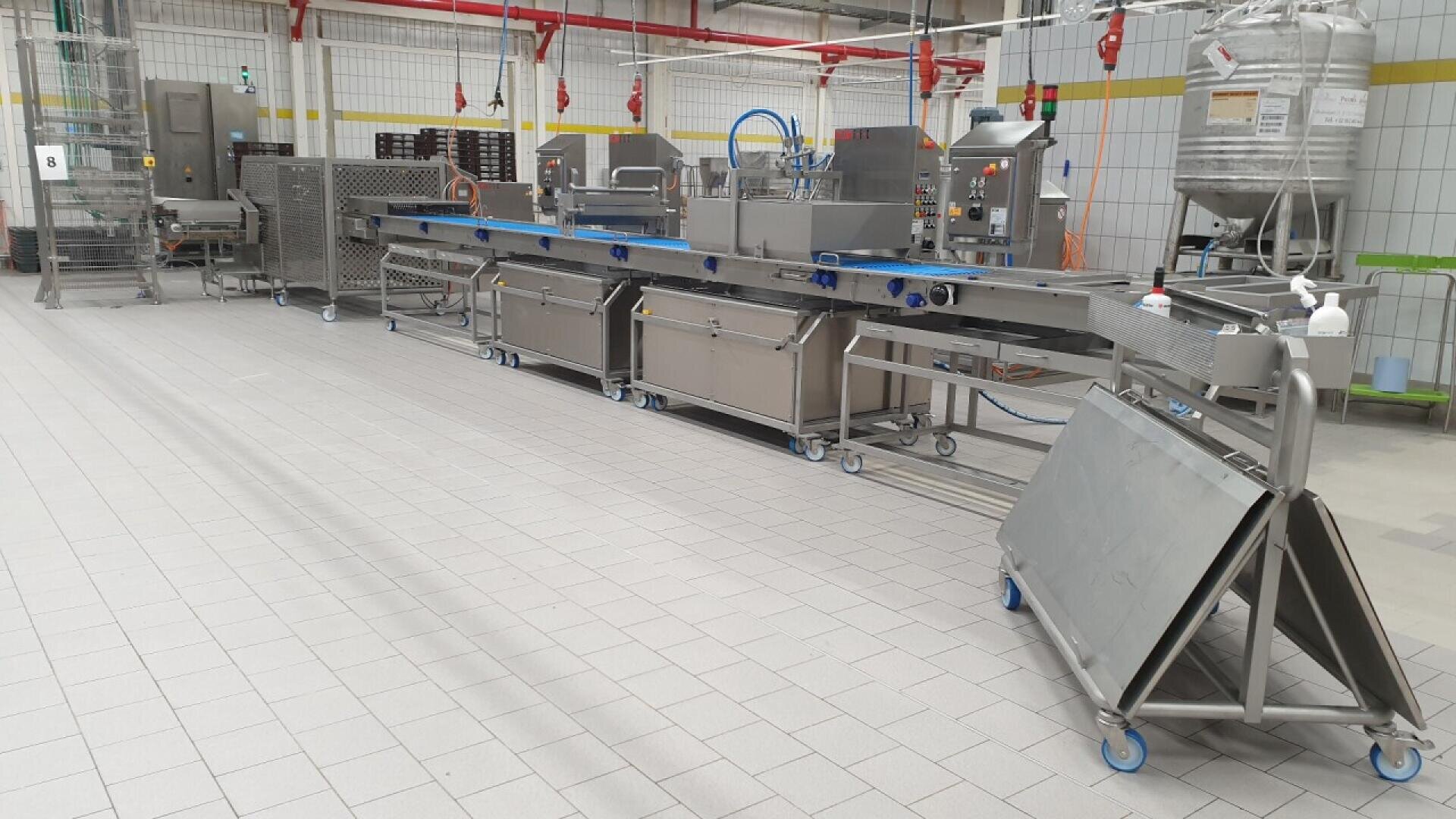 A modern industrial food processing machine with conveyor belts and stainless steel equipment in a clean, tiled factory setting.