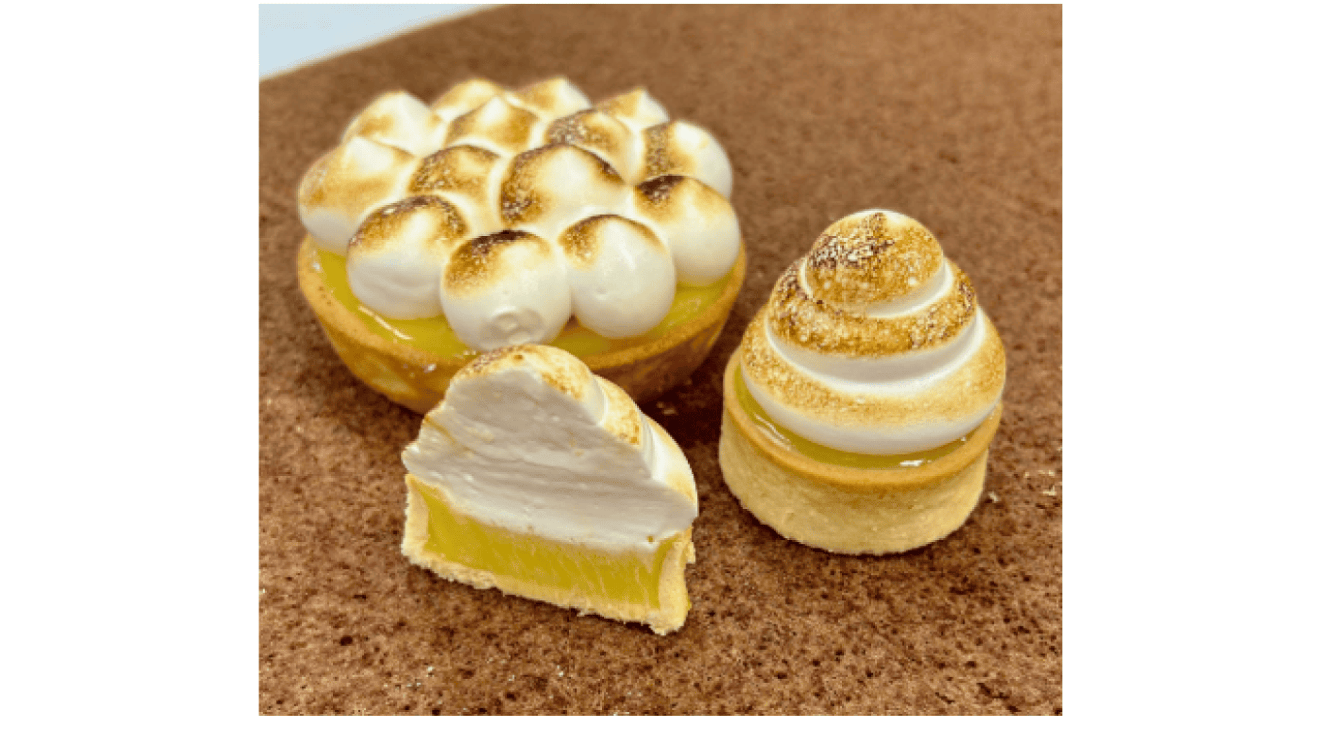 Three lemon meringue tarts on a brown surface: one topped with round meringue peaks, one sliced to show yellow filling, and one with a swirled meringue topping.