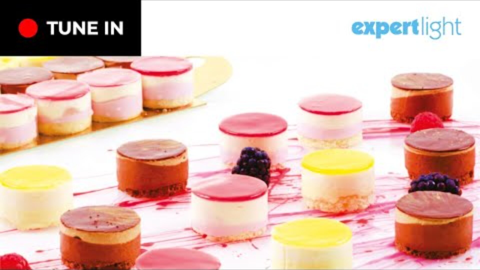 A selection of colorful mini layer cakes with a glossy finish, arranged on a white surface with berry garnish. The TUNE IN and Expert Light logos appear in the corners.