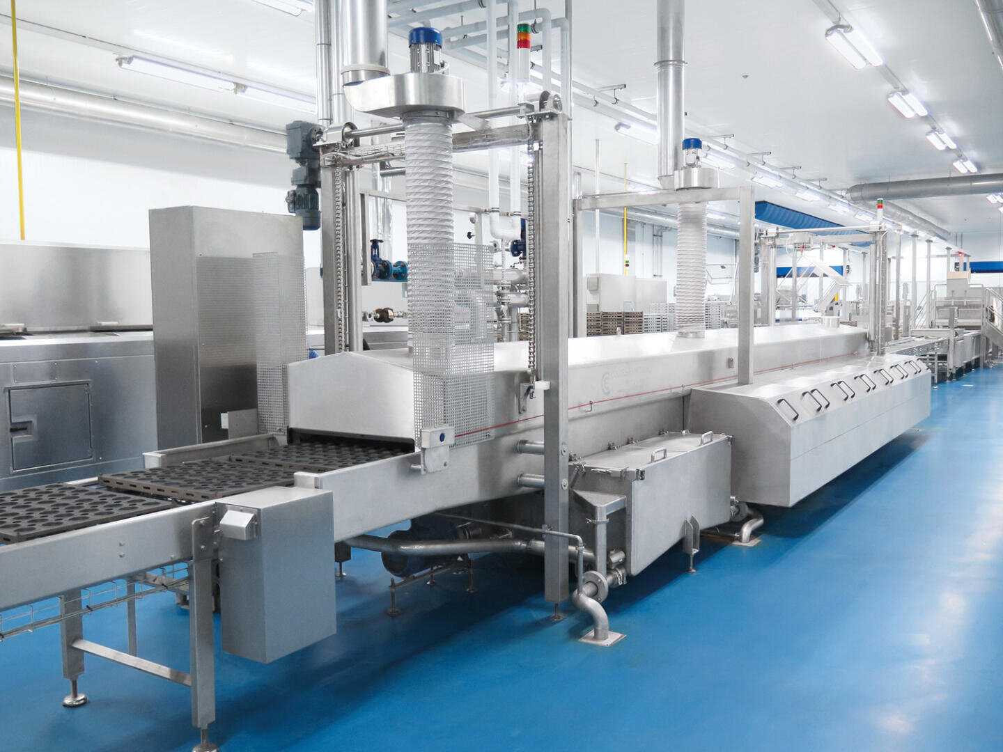 Eine moderne, automatisierte Produktionslinie zur Lebensmittelverarbeitung mit Maschinen und Förderbändern aus Edelstahl in einer sauberen, hell erleuchteten Fabrik mit blauem Boden.