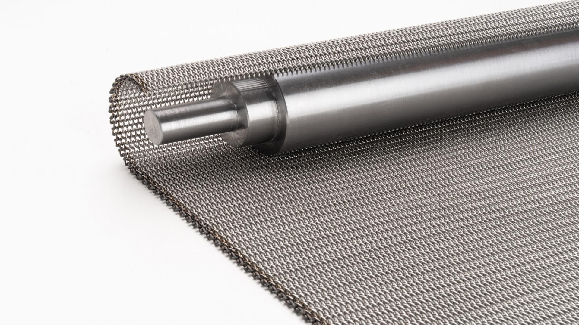 A close-up of a metal mesh conveyor belt partially unrolled, with a cylindrical metal roller on a white background.