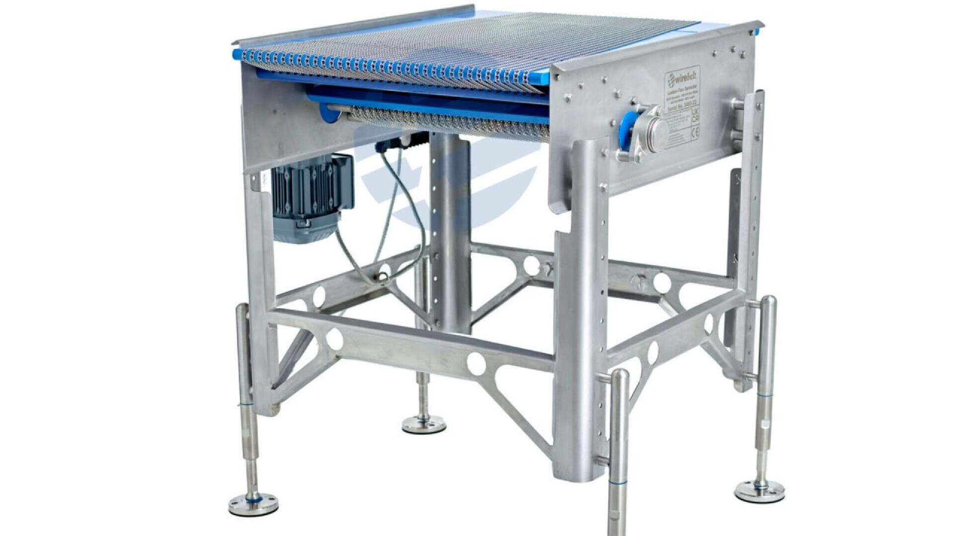 A stainless steel industrial conveyor belt machine with adjustable legs, a flat metal mesh belt, an electric motor, and control components. The equipment is designed for material or food processing in factories.