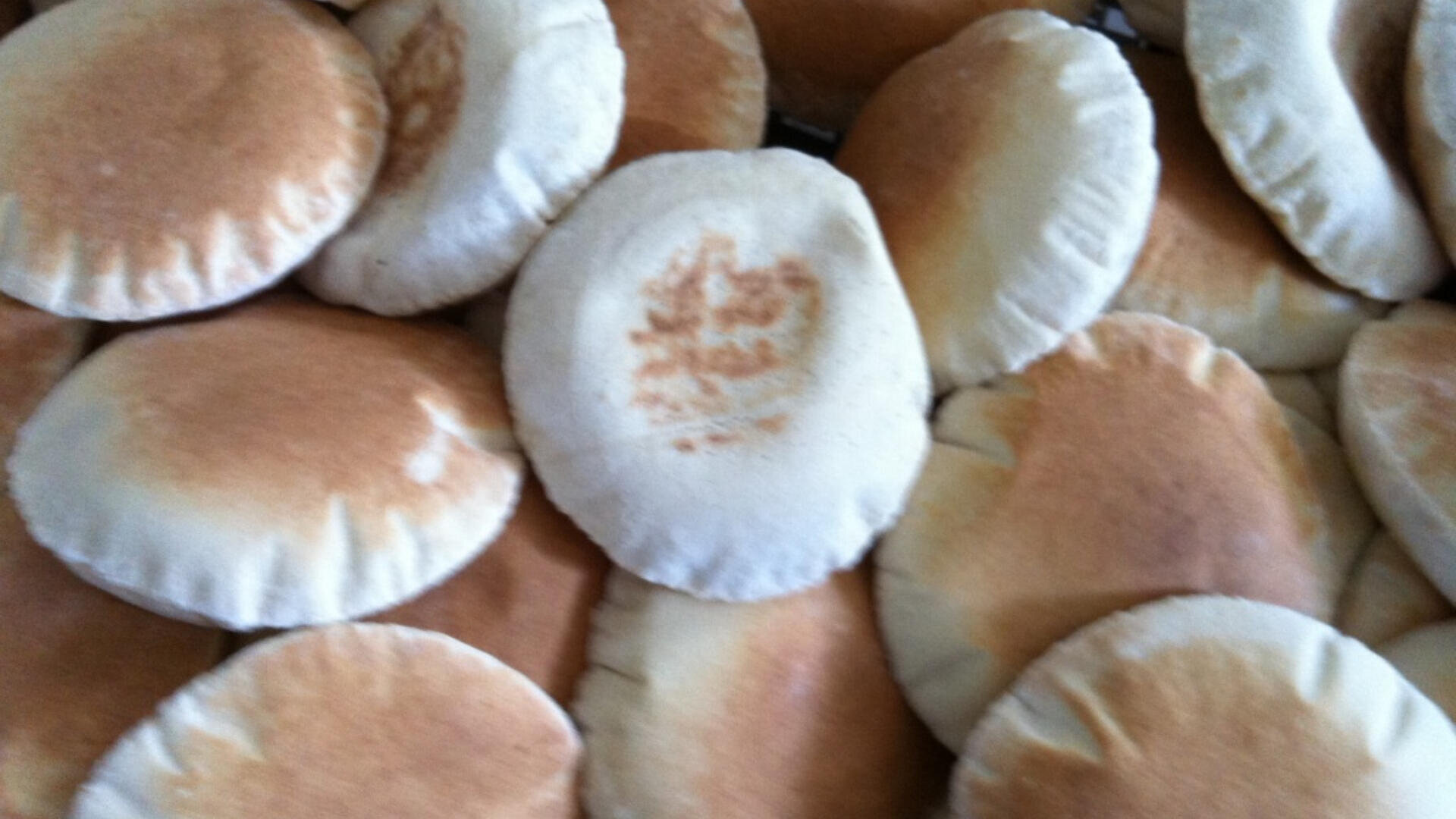 A close-up view of several round pita breads with golden-brown tops stacked closely together, showing their soft, puffy texture.