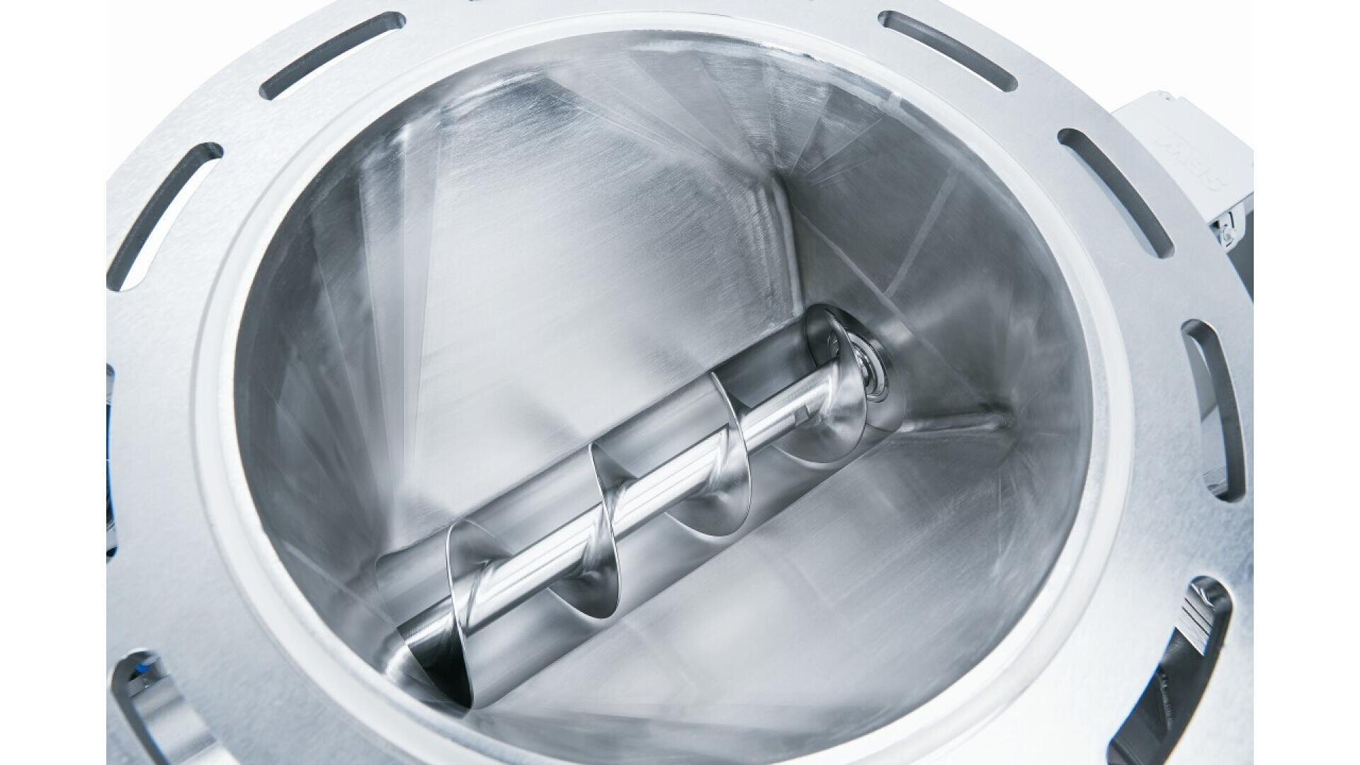Close-up view of the inside of a shiny, metallic industrial mixer or processing machine, featuring a polished spiral auger or screw conveyor at the center.