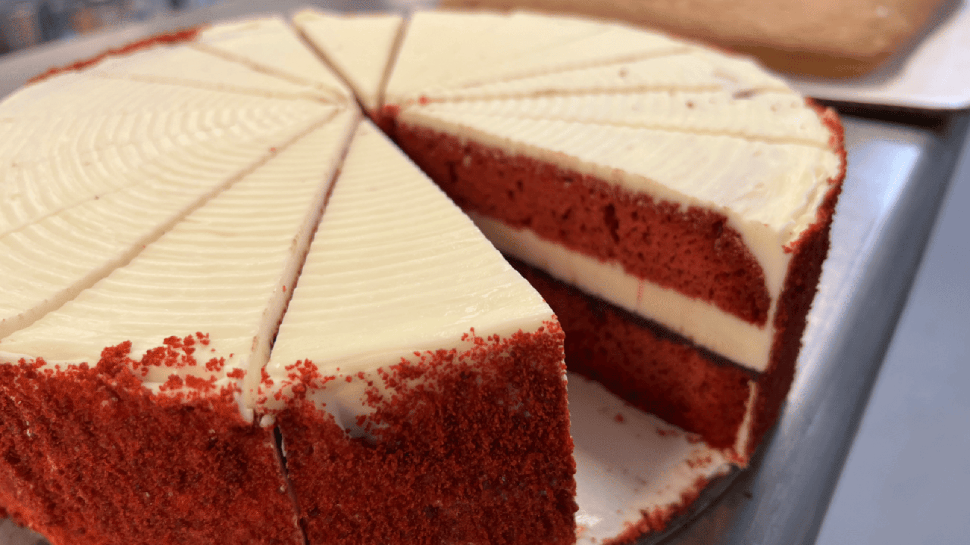 Nahaufnahme einer in Scheiben geschnittenen roten Samttorte mit Frischkäseglasur, die zwei Schichten aus rotem Kuchen und weißer Glasur zeigt. Ein Stück ist leicht aus der ganzen Torte herausgezogen.