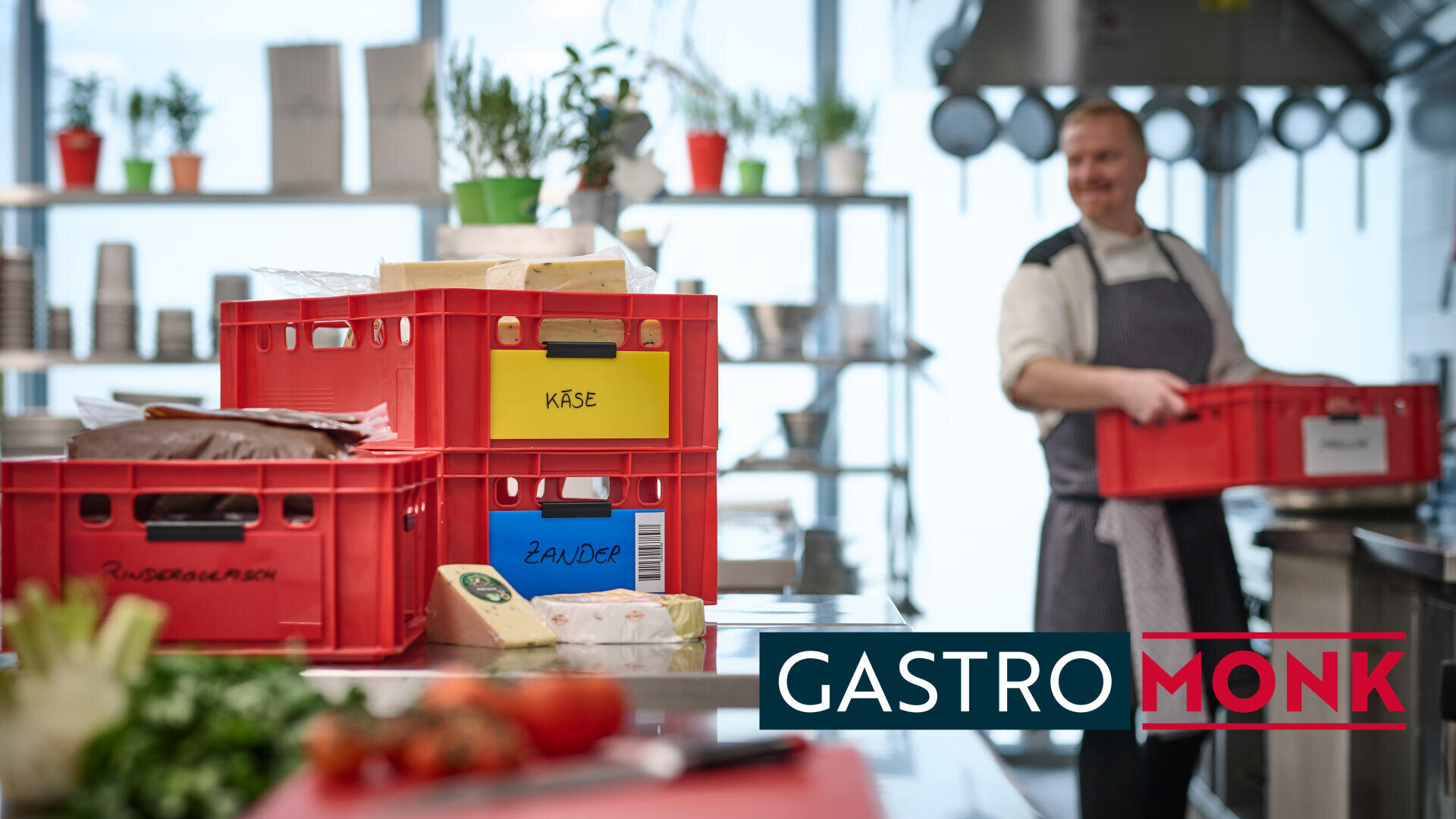 A chef in a kitchen holds a red crate, surrounded by stacked crates labeled “Käse” and “Zander.” Fresh vegetables are on the counter, and “GASTROMONK” is written in bold text at the bottom.