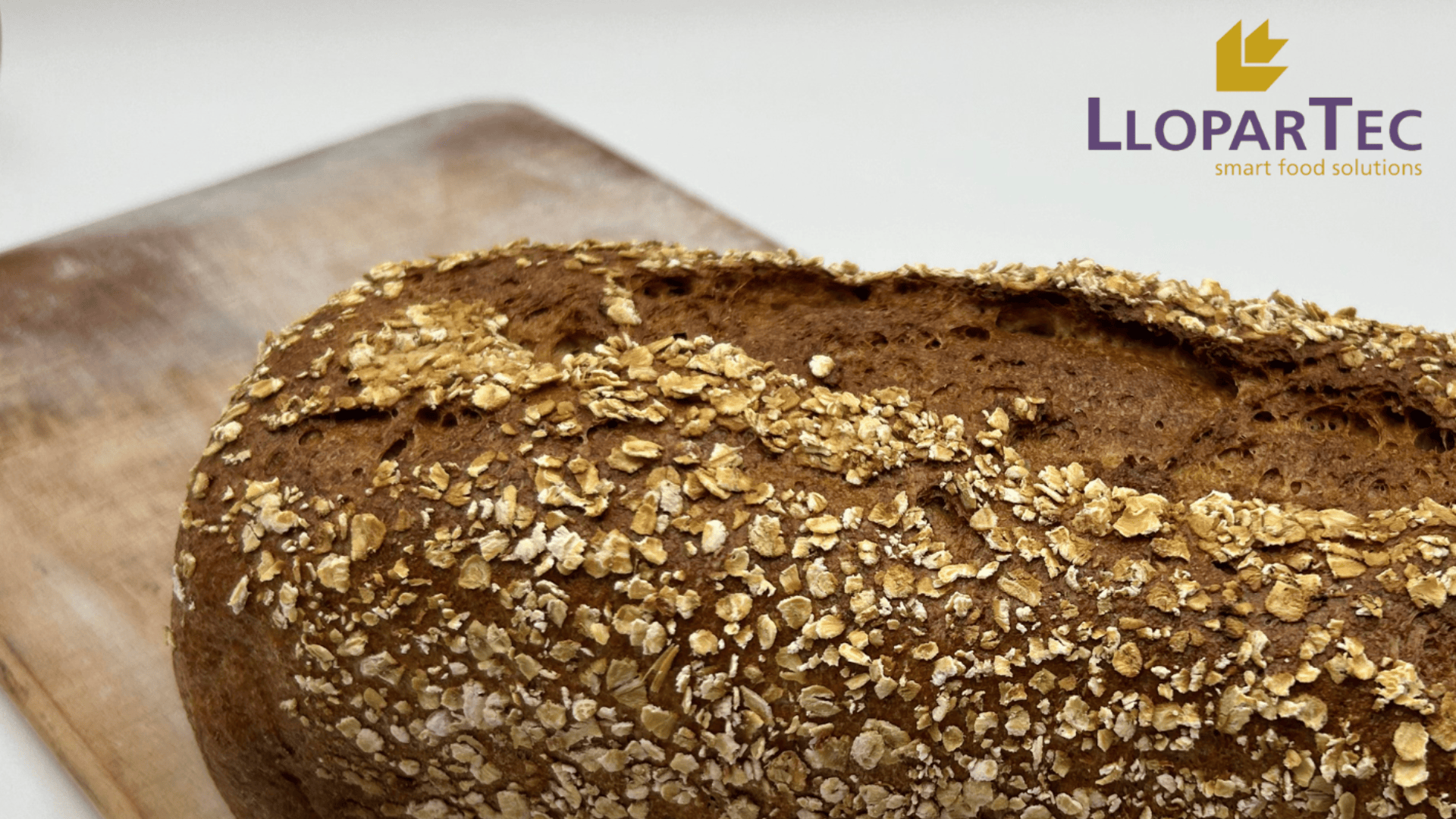A loaf of whole grain bread topped with oats rests on a wooden board. The background is white, and the LloparTec logo with the phrase smart food solutions appears in the top right corner.