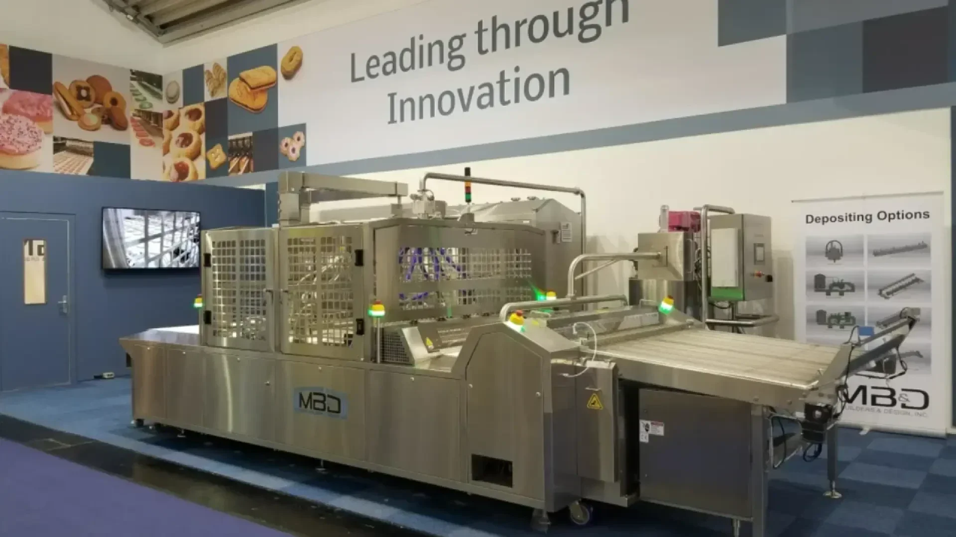 Eine große, industrielle Lebensmittelverarbeitungsmaschine ist auf einer Ausstellung ausgestellt, darüber ein Schild mit der Aufschrift Führend durch Innovation. Im Hintergrund sind Bilder von Lebensmitteln und eine Tabelle mit Pfandoptionen zu sehen.
