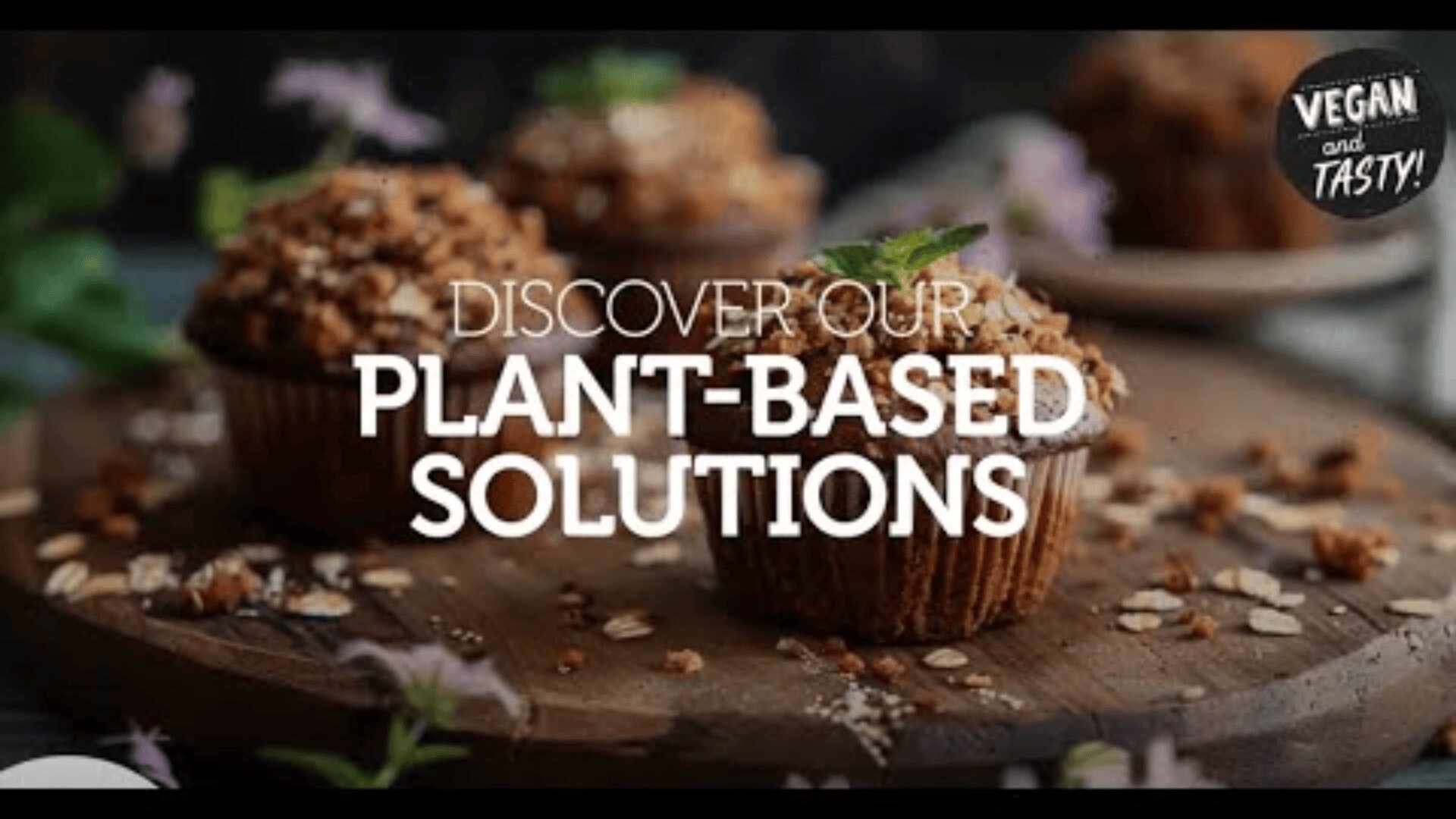A wooden board with vegan muffins topped with oats and herbs. The text Discover our plant-based solutions is overlaid, and a badge in the corner reads Vegan and tasty!.
