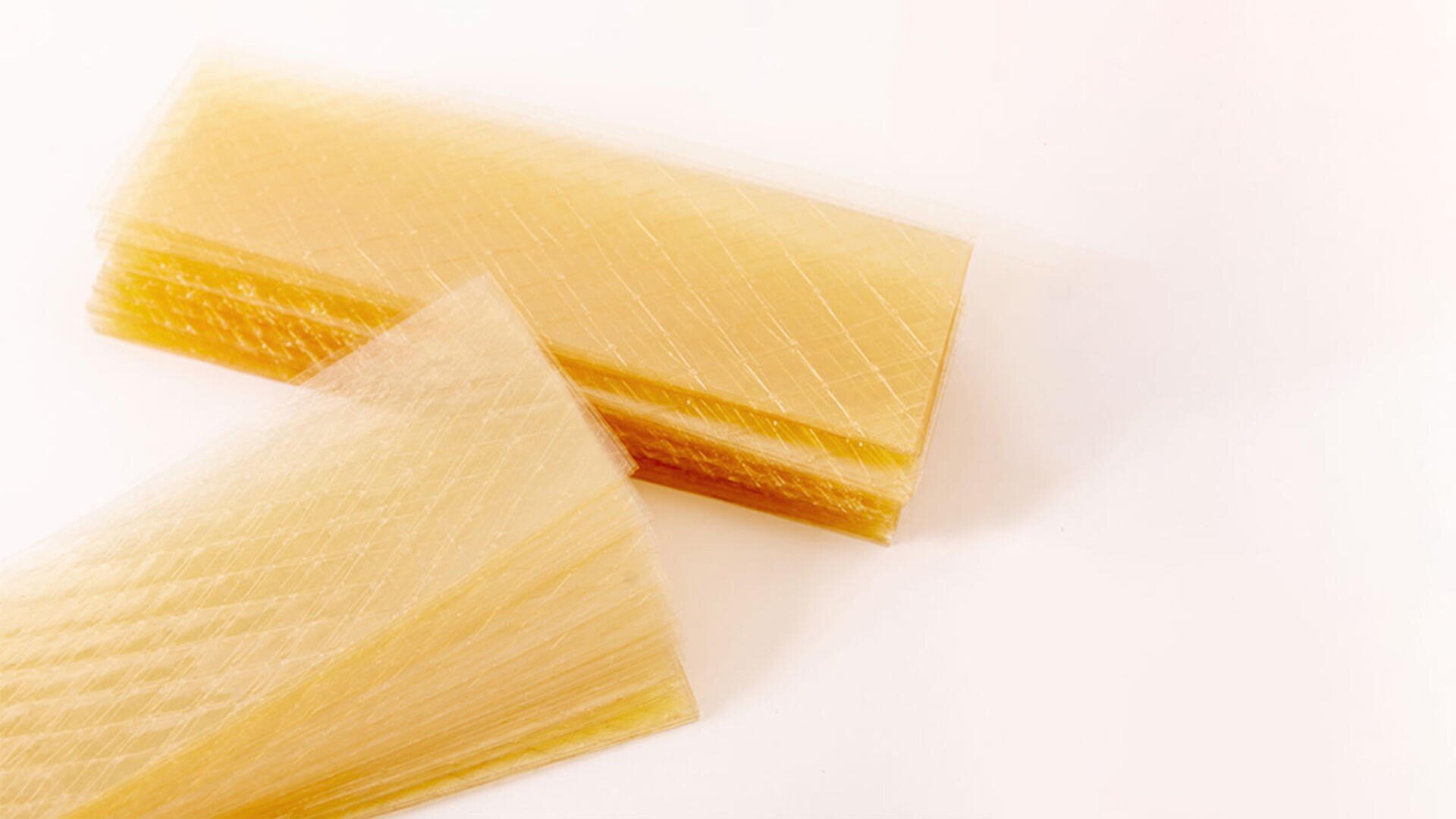 Rectangular sheets of yellowish gelatin with a crisscross pattern, stacked and overlapping on a white surface.