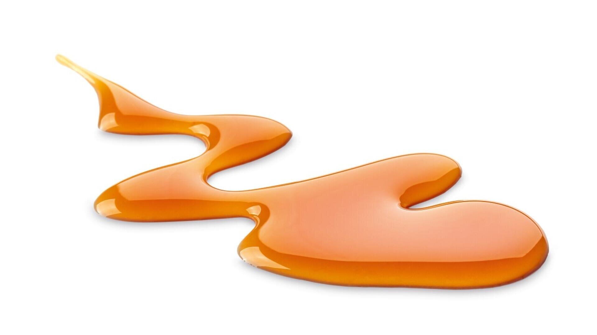 A glossy stream of golden brown caramel sauce spreads across a white background in a wavy pattern, creating a shiny and appetizing appearance.