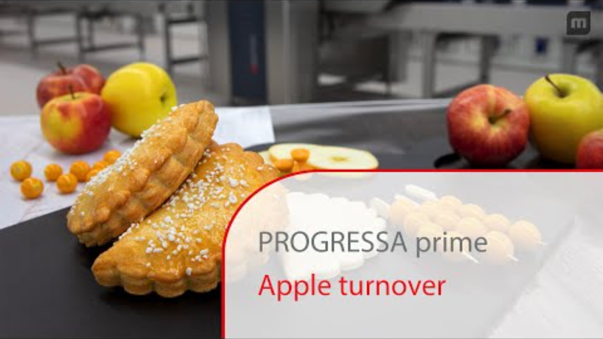 Two apple turnovers sprinkled with sugar sit on a black tray, surrounded by fresh apples and sliced apples. A blurred background shows a modern kitchen or bakery setting. Text on the image reads, PROGRESSA prime Apple turnover.