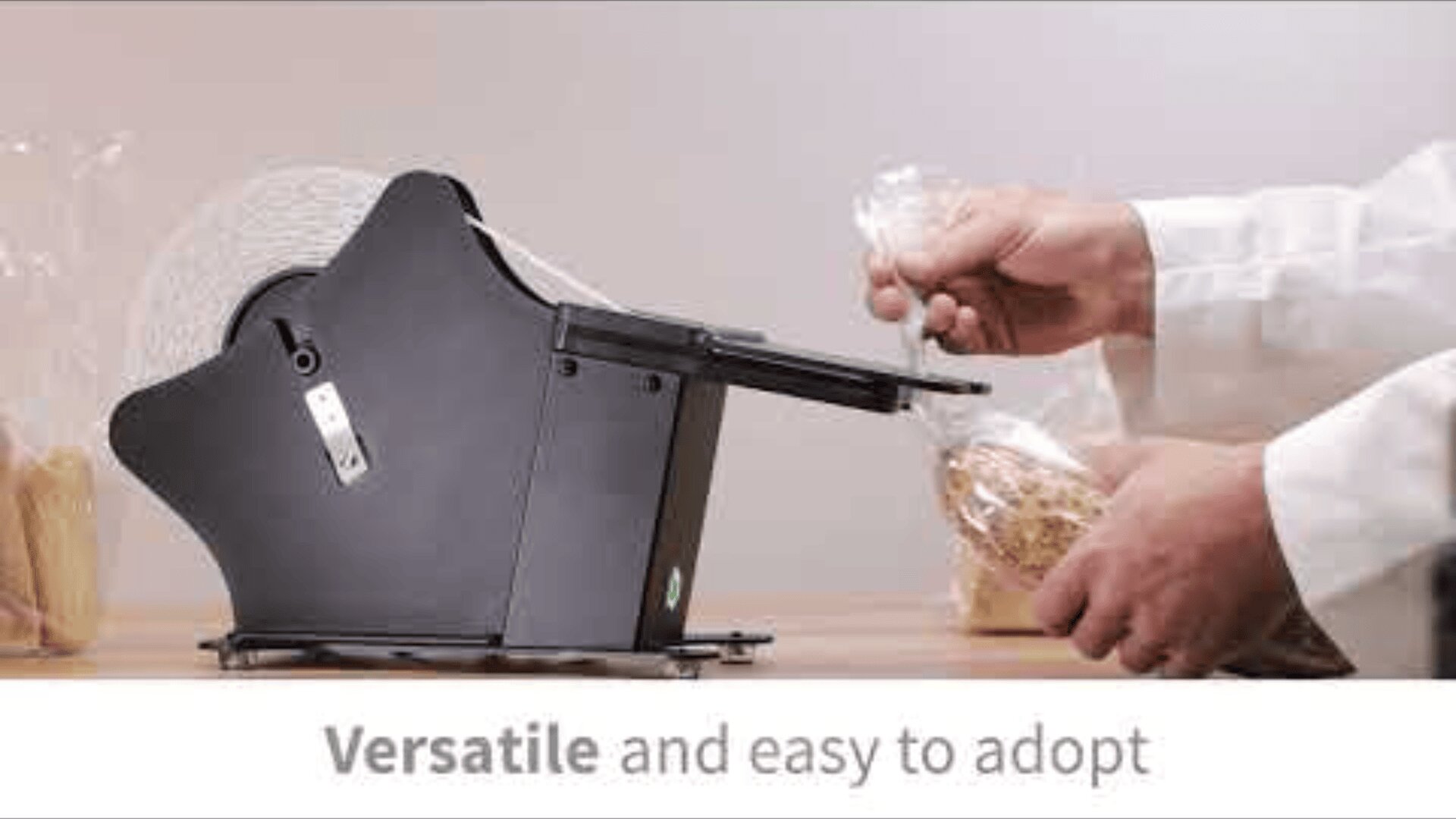 A person uses a black tape dispenser to seal a plastic bag of food on a wooden surface. Text below reads, Versatile and easy to adopt.
