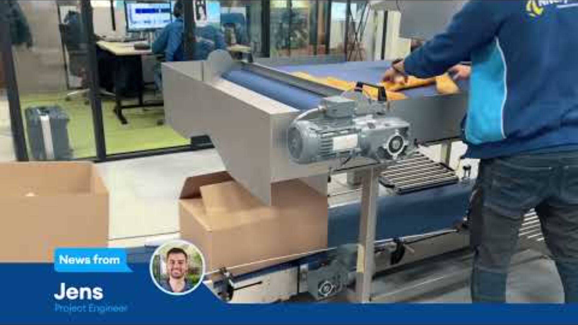 A person in a blue jacket works at a conveyor belt, placing items into a box. In the background, people are visible through glass walls in an office setting. A lower-third graphic introduces Jens, Project Engineer.