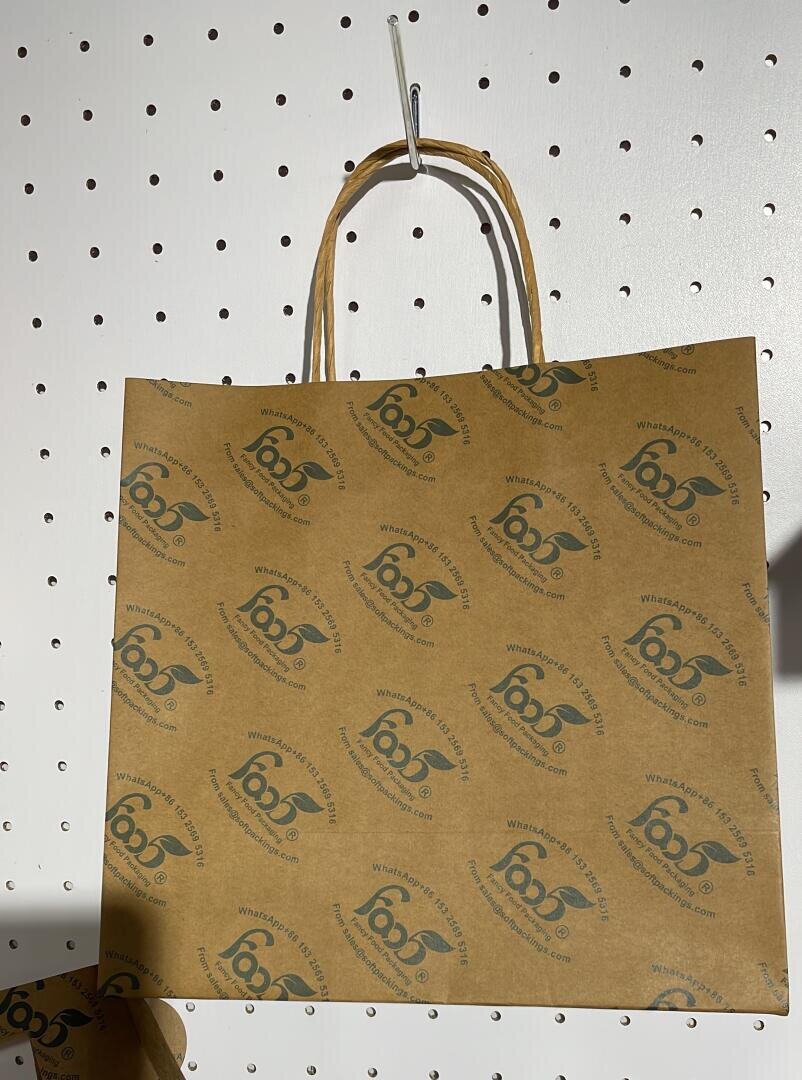 A brown paper shopping bag with twisted handles hangs on a pegboard wall. The bag features a repeating black logo and the words 66°North printed diagonally across the surface.