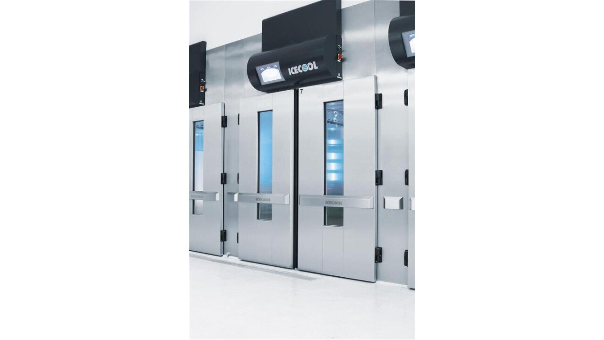 A row of modern, stainless steel industrial freezer doors with rectangular windows and blue-lit interiors, set against a clean white floor and walls. One door has a sign reading KEGEL.