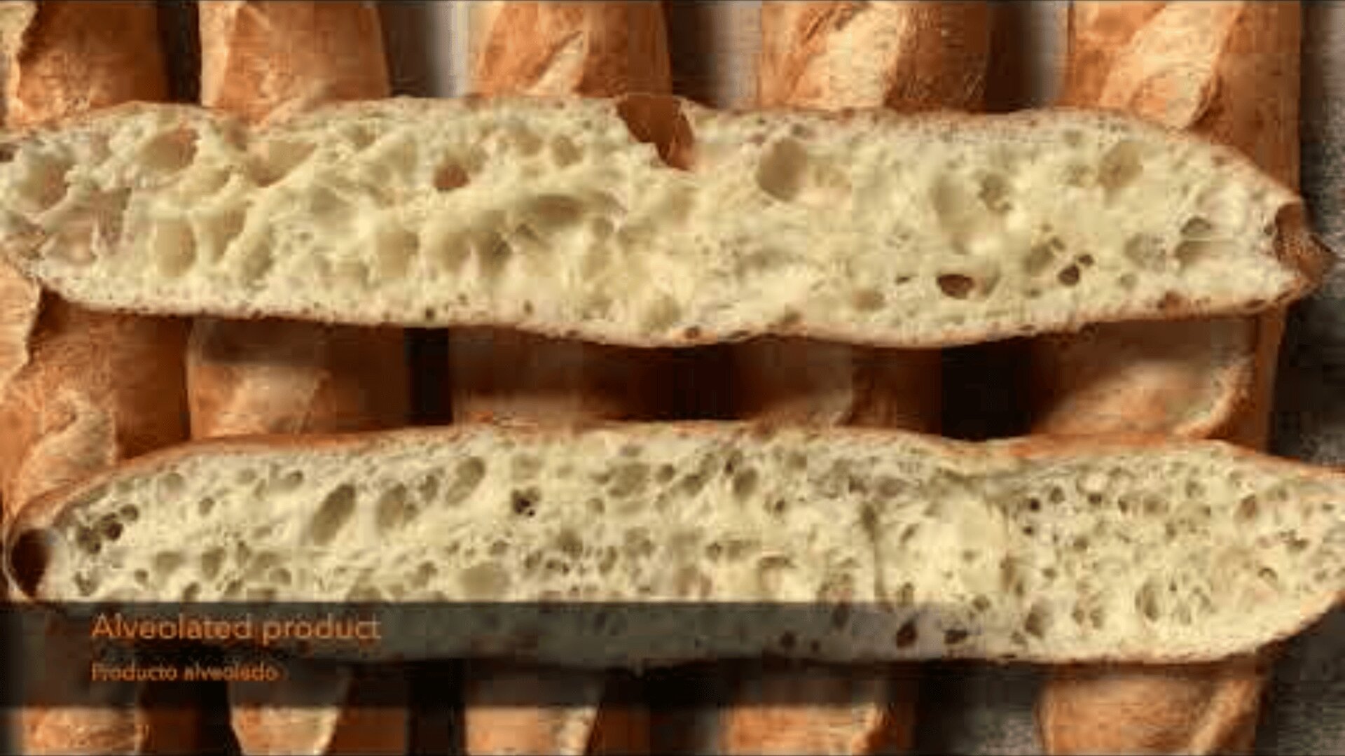 Two sliced baguettes with an open crumb and visible air pockets rest on several whole baguettes. Text in the corner reads: Alveolated product. Producto alveolado.